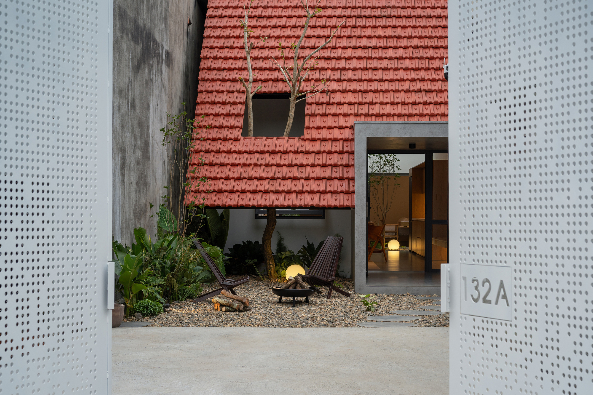 View through perforated white metal entry gates toward the red tile roof and courtyard beyond
