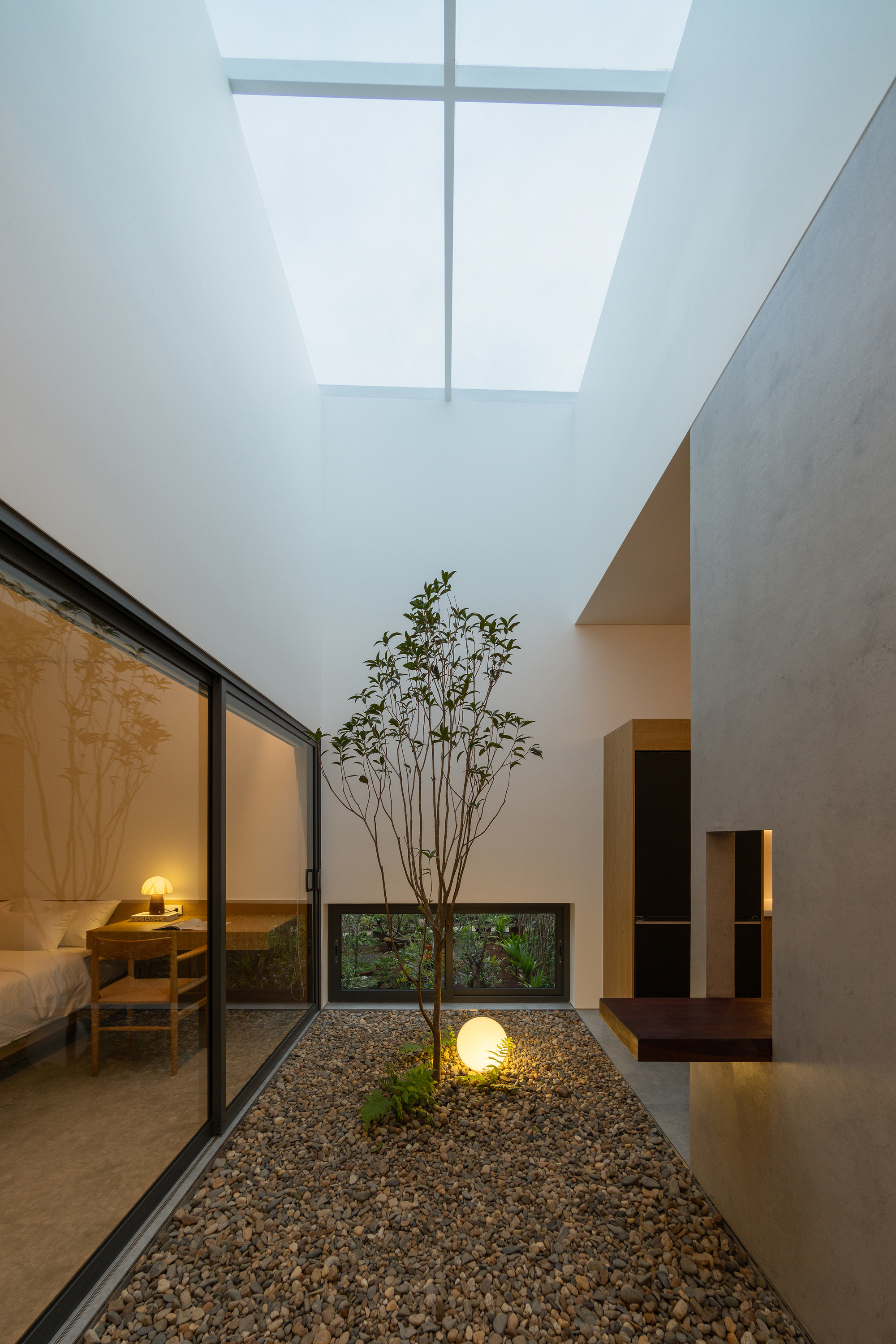 Interior courtyard with gravel bed and slender tree beneath a skylight at dusk