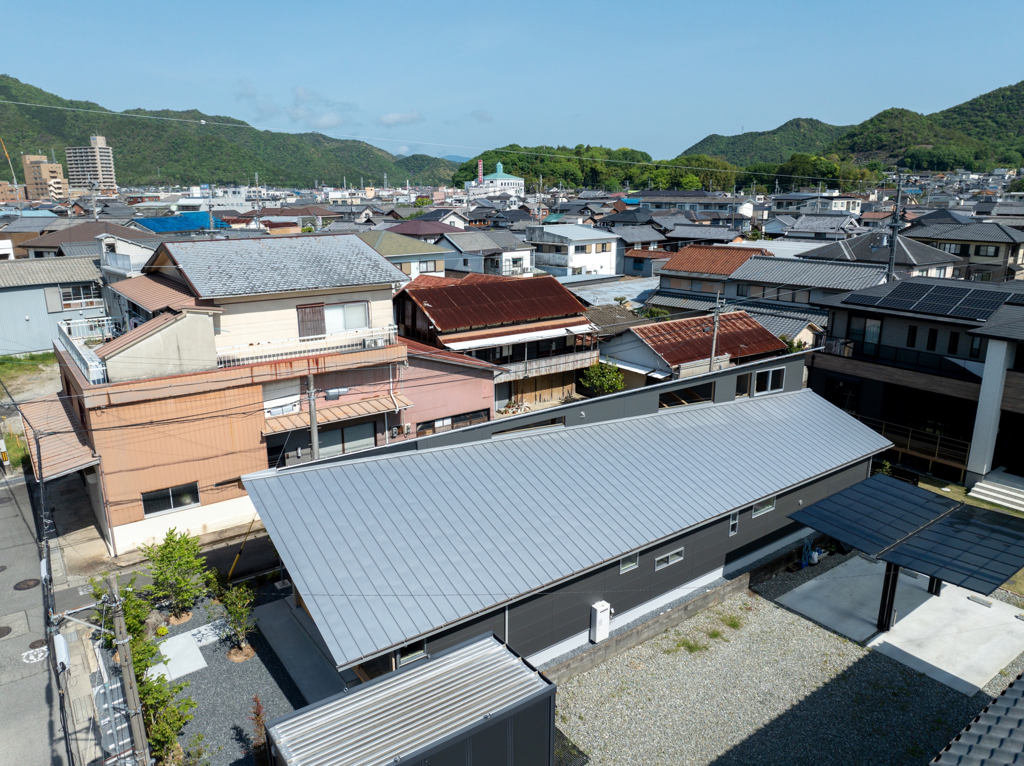 Aerial view of the corrugated metal roof nestled among neighboring residences with mountains beyond