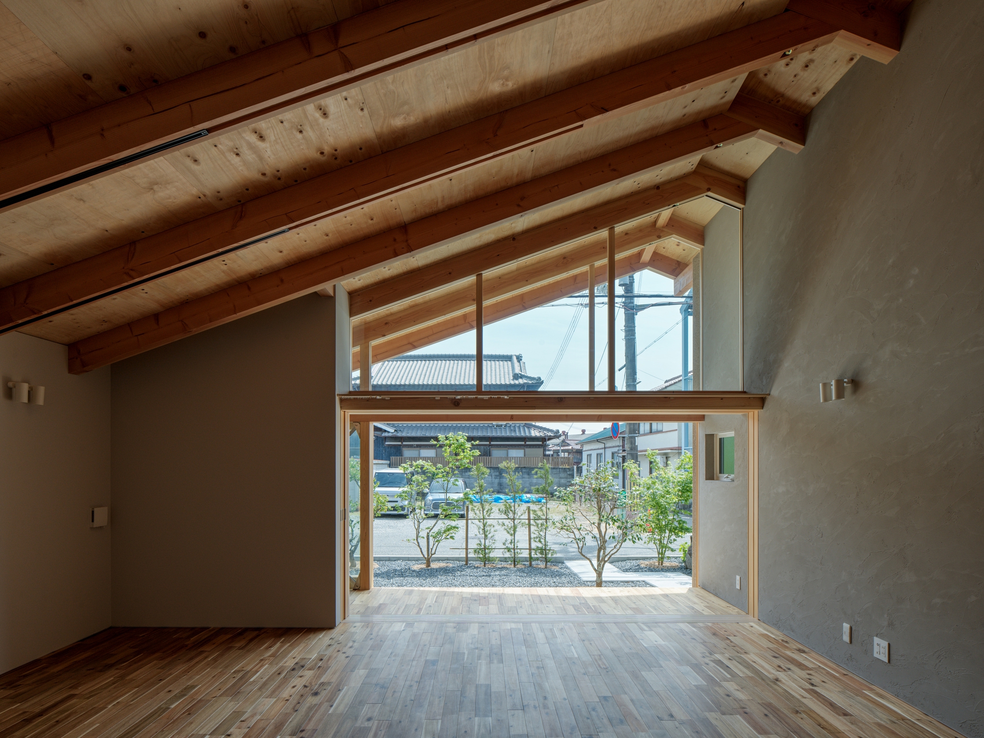 Interior view through the timber-framed opening toward the planted courtyard with young trees in daylight
