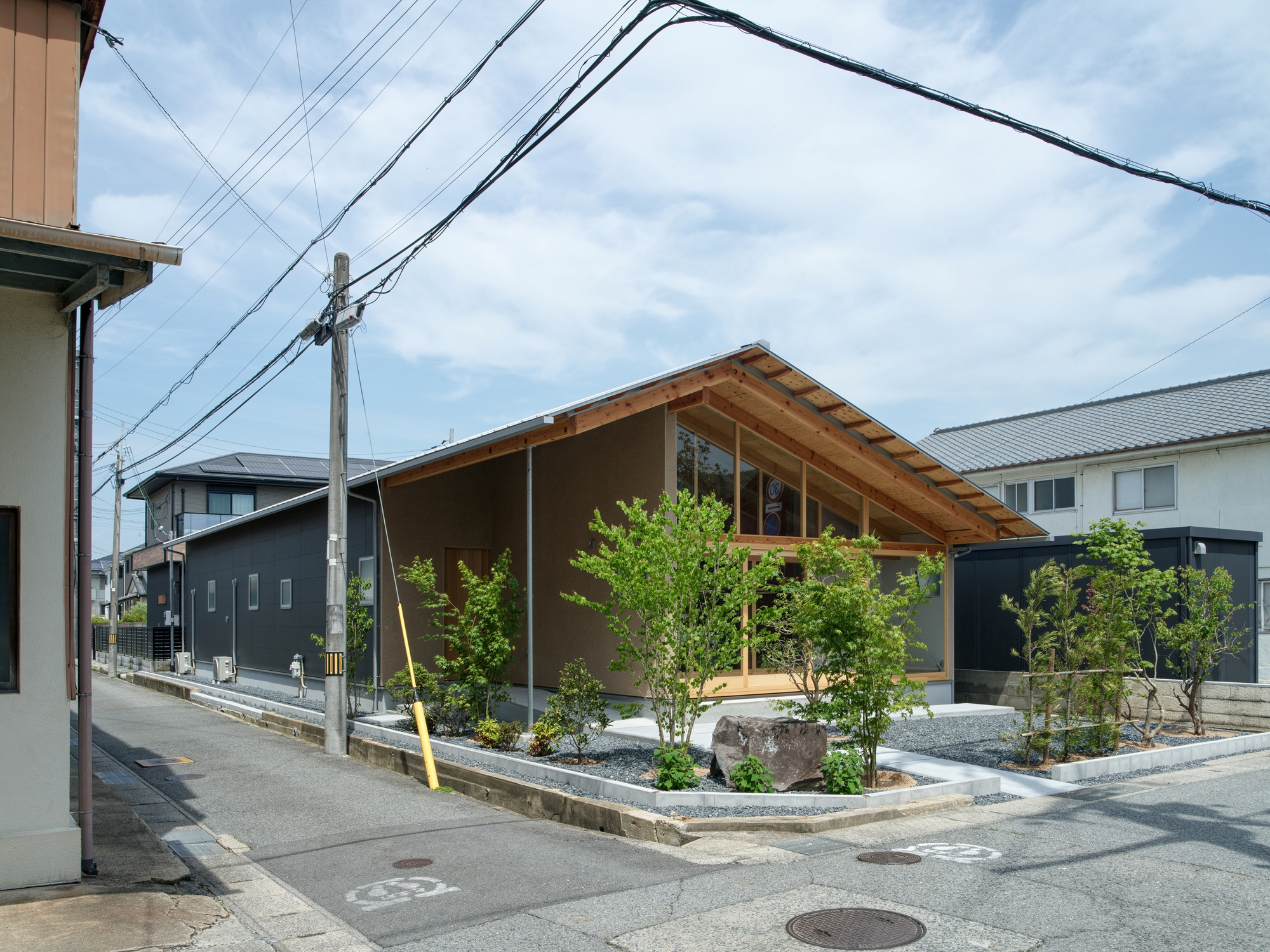 Street view of a low-slung residence with exposed timber roof and planted front courtyard under cloudy sky