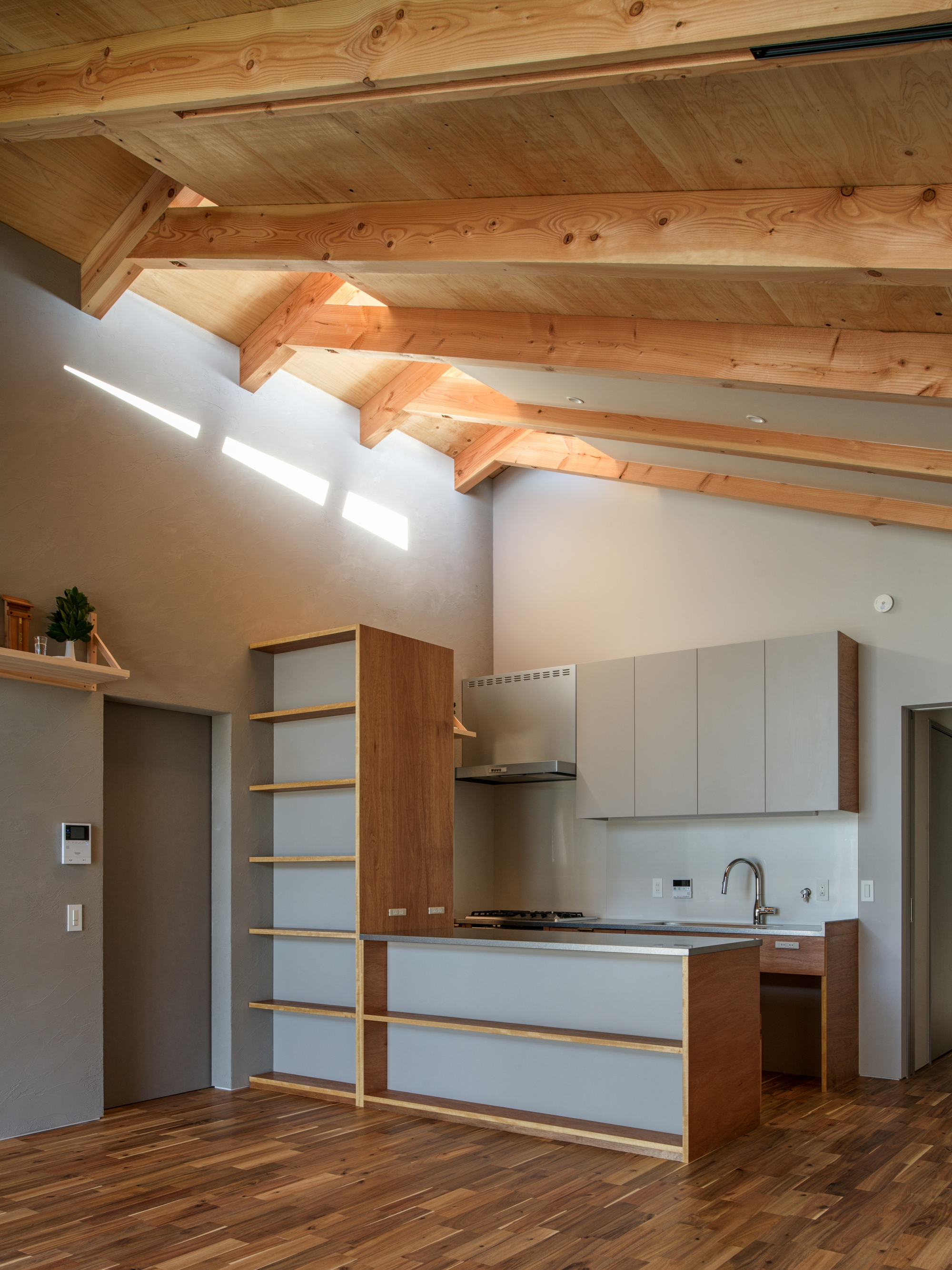 Kitchen galley with timber and white cabinetry below exposed rafters and a clerestory window slot