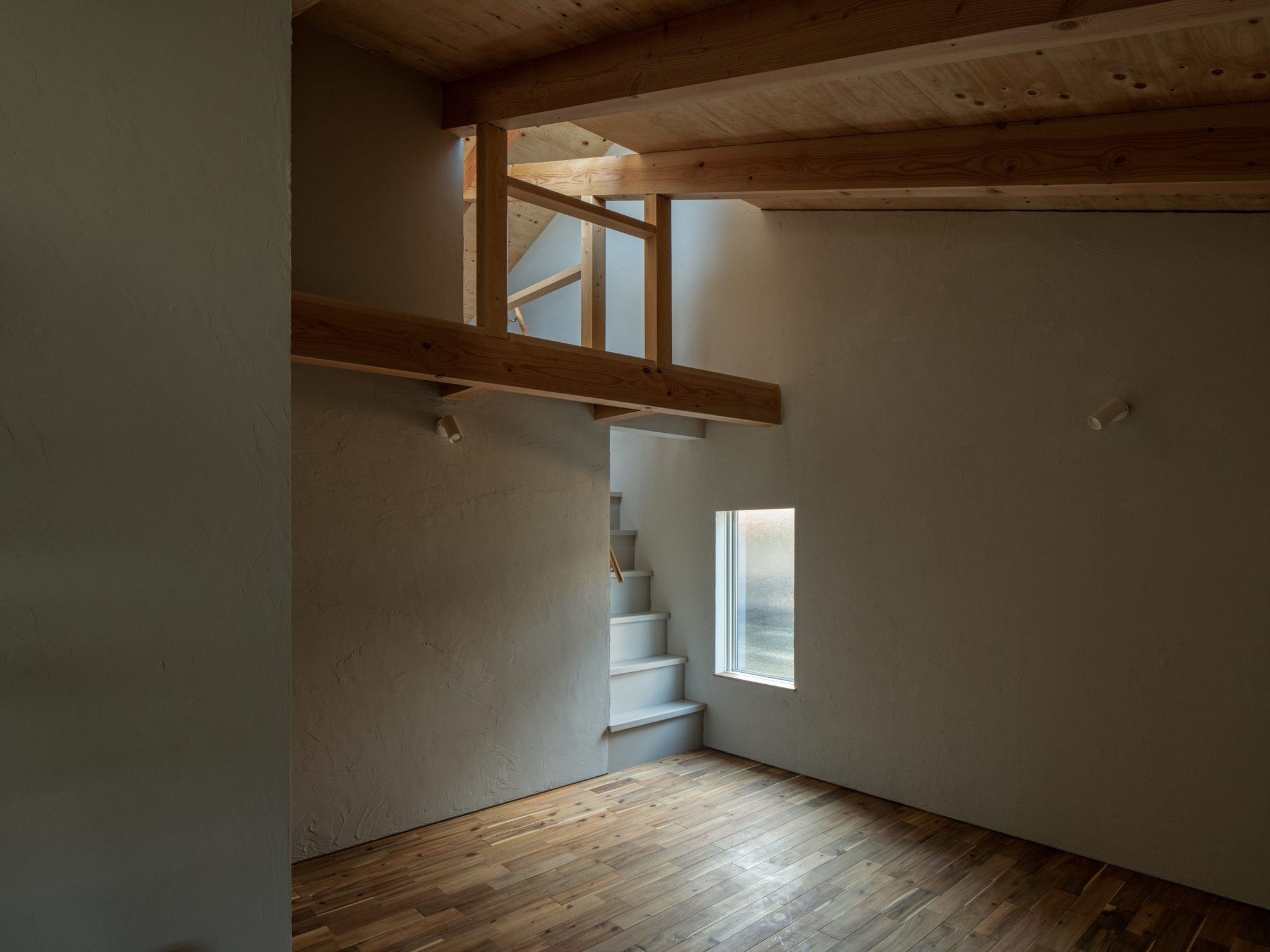 Folded metal staircase ascending toward timber loft with exposed beams and natural light from above