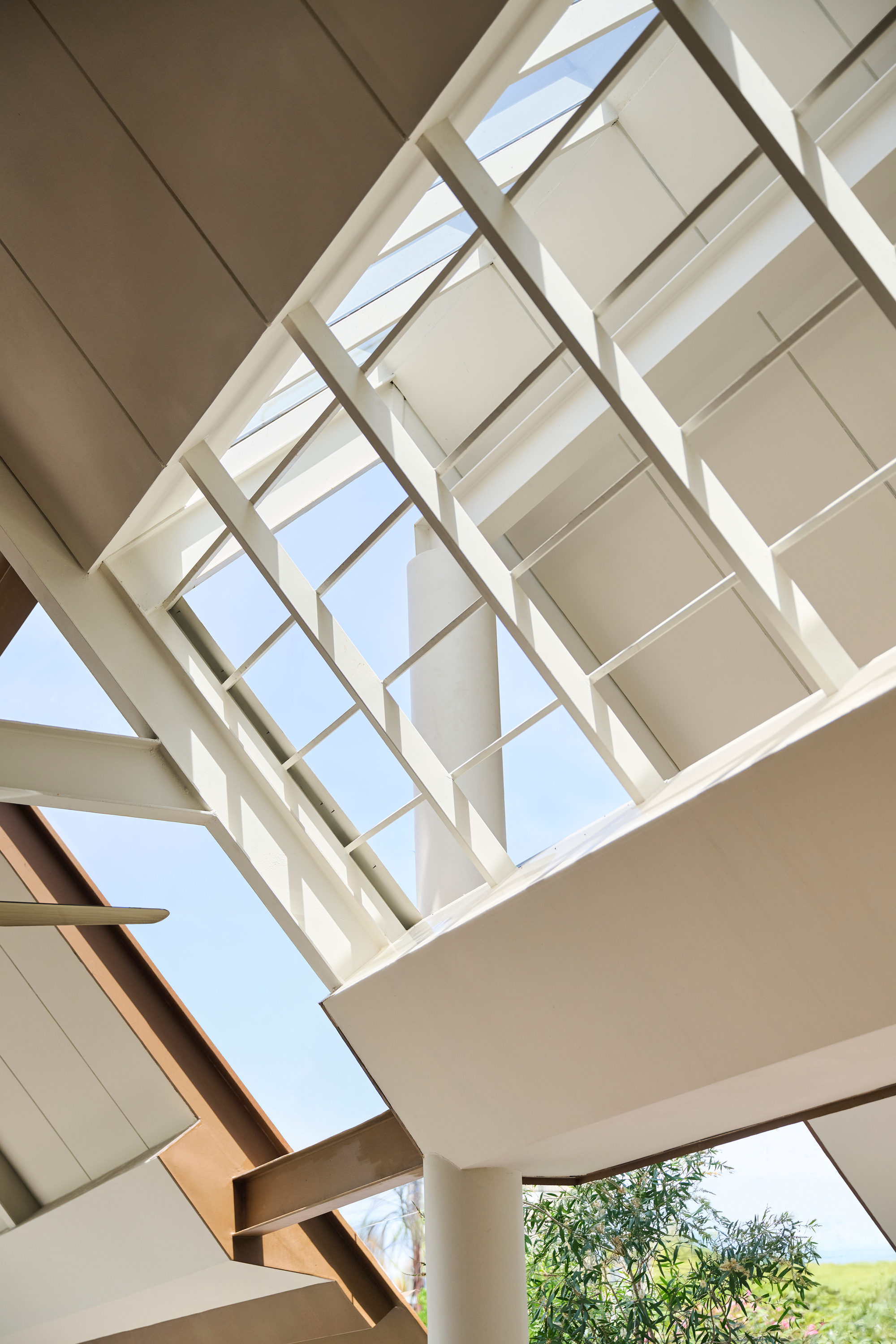 Upward view through timber-framed skylight with geometric glazing and potted plants on upper level