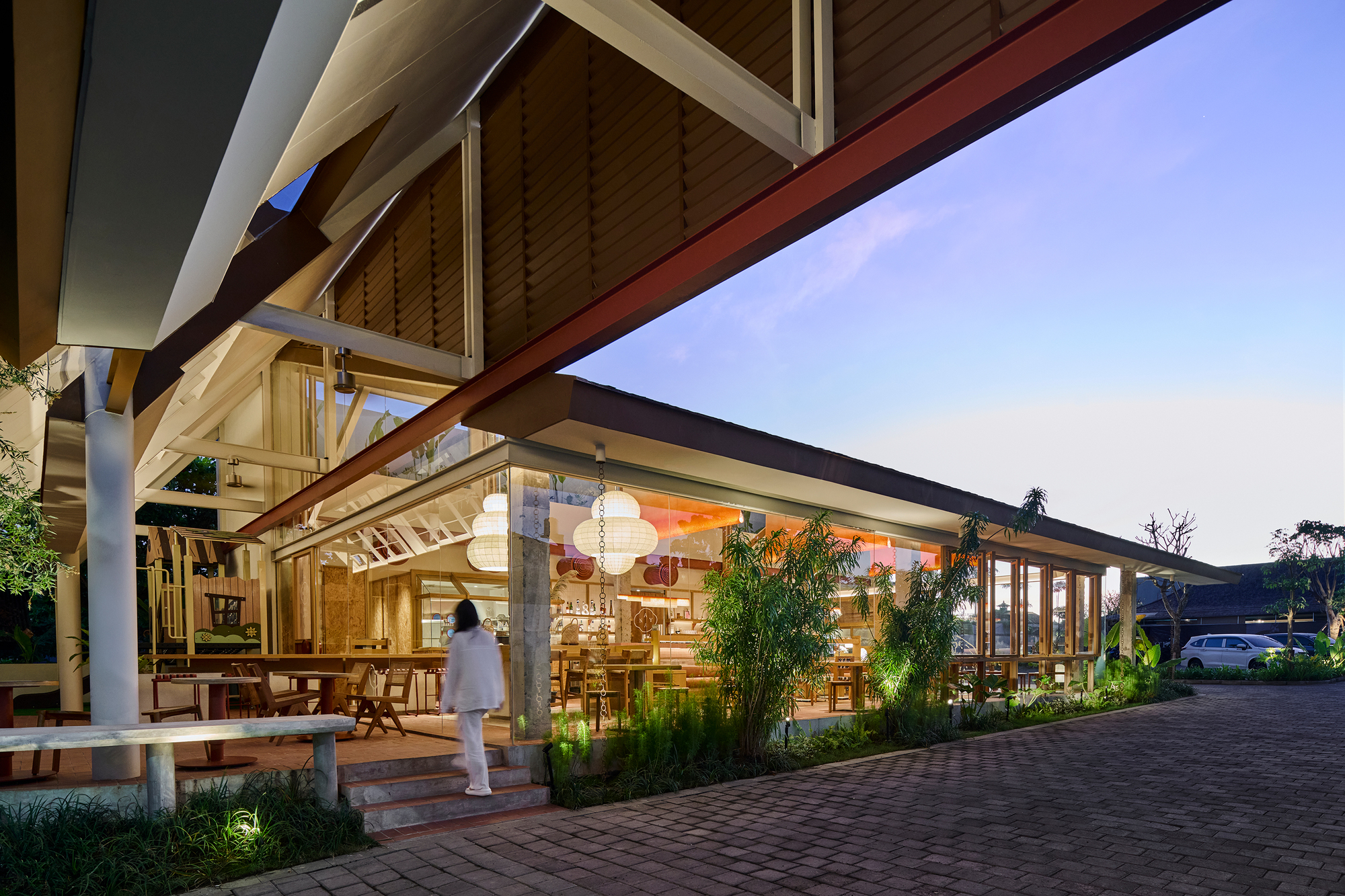 Covered entrance canopy with exposed timber beams and wood ceiling above planted beds at dusk