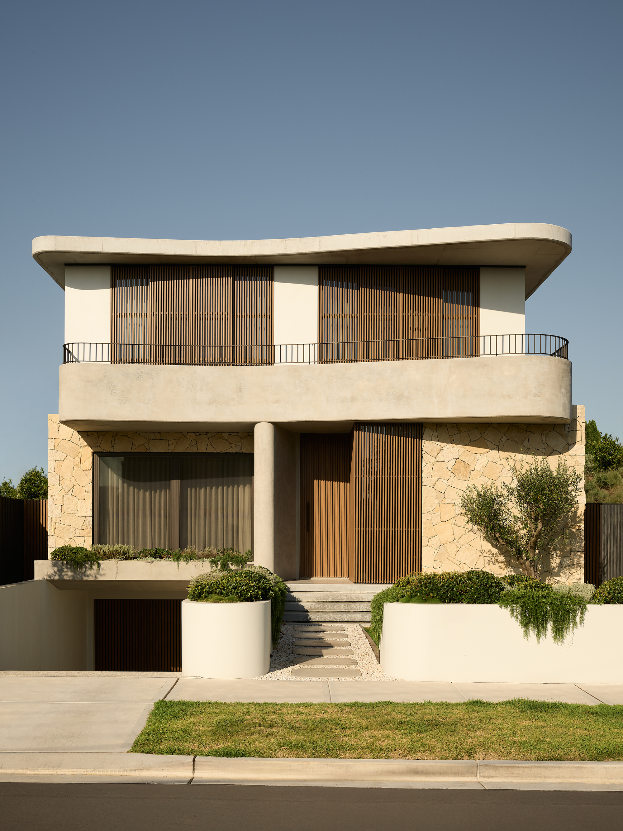 Street view of the two-story facade with vertical timber screens and stone base beneath a curved roof