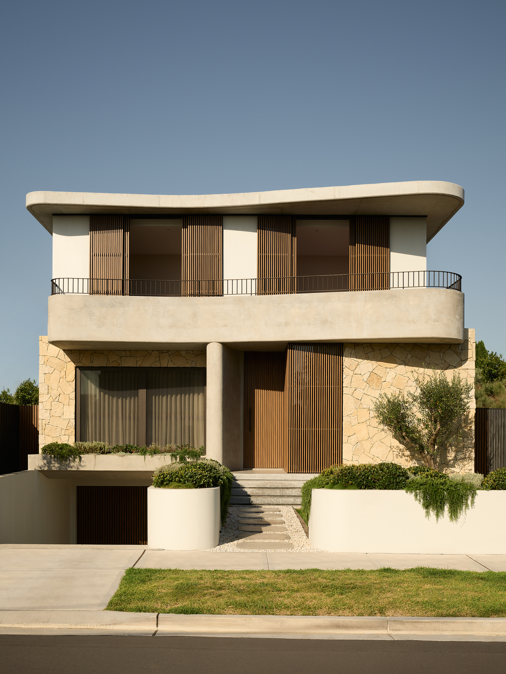 Front elevation showing timber shutters opened on the upper level balcony under clear blue sky