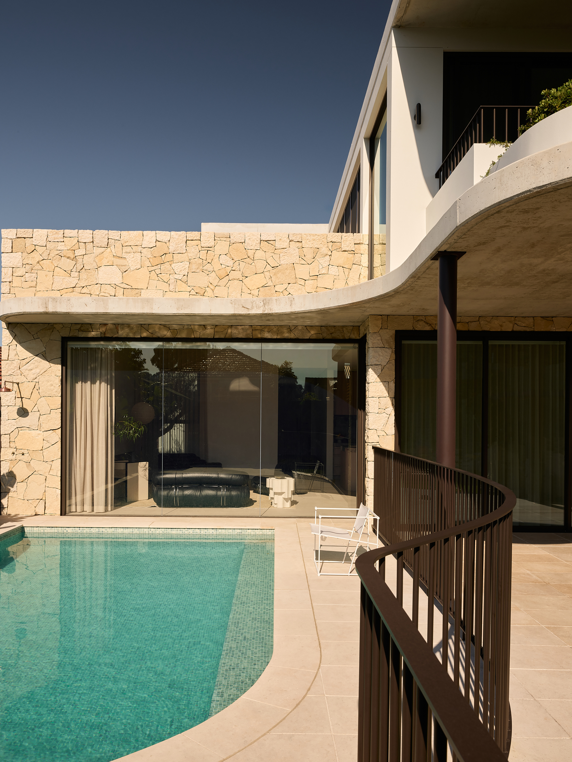 Pool terrace with curved stone wall and spiral balustrade beneath cantilevered upper floor