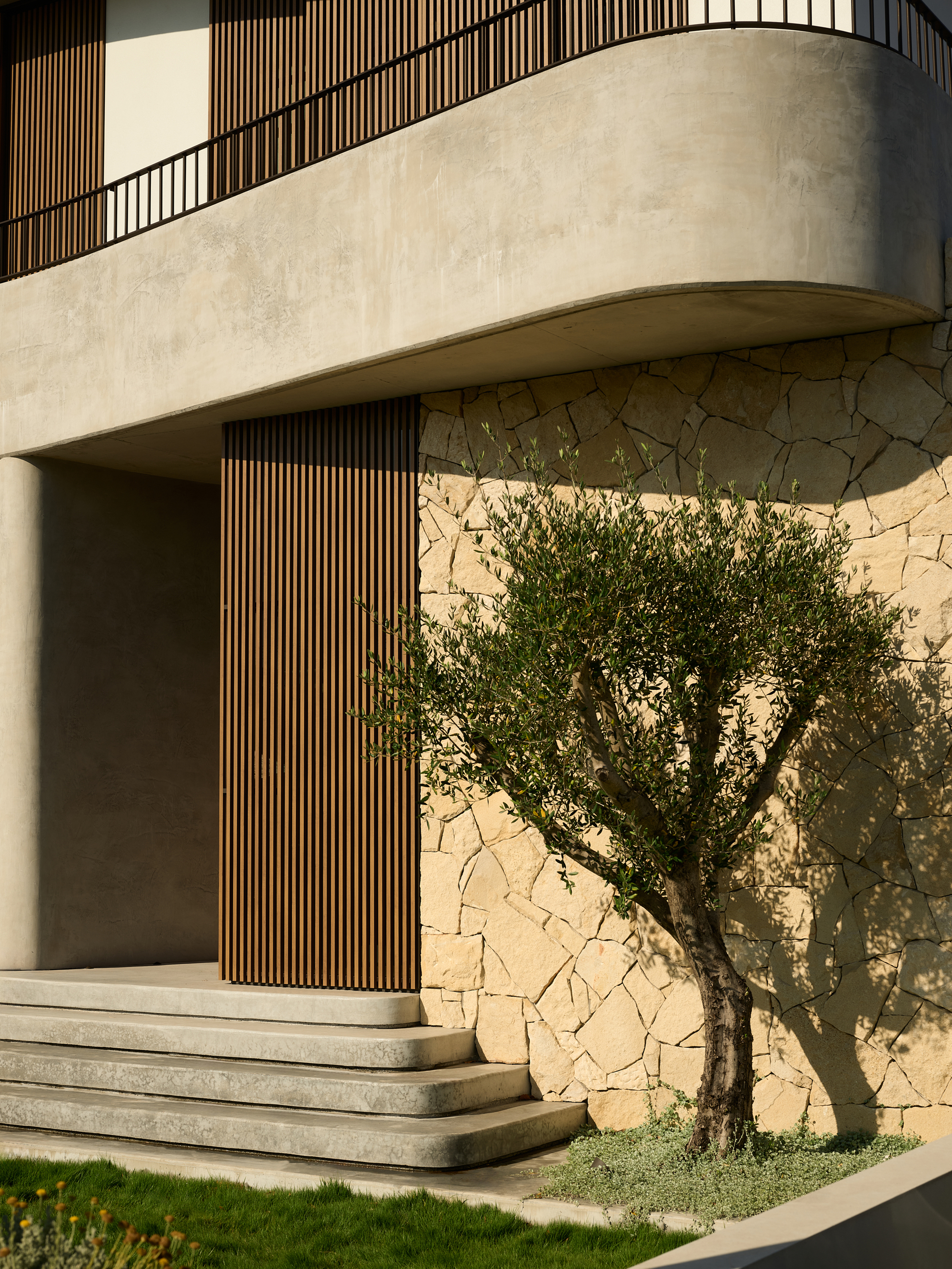Close-up of the curved balcony edge meeting the stone wall with an olive tree casting shadows on the facade