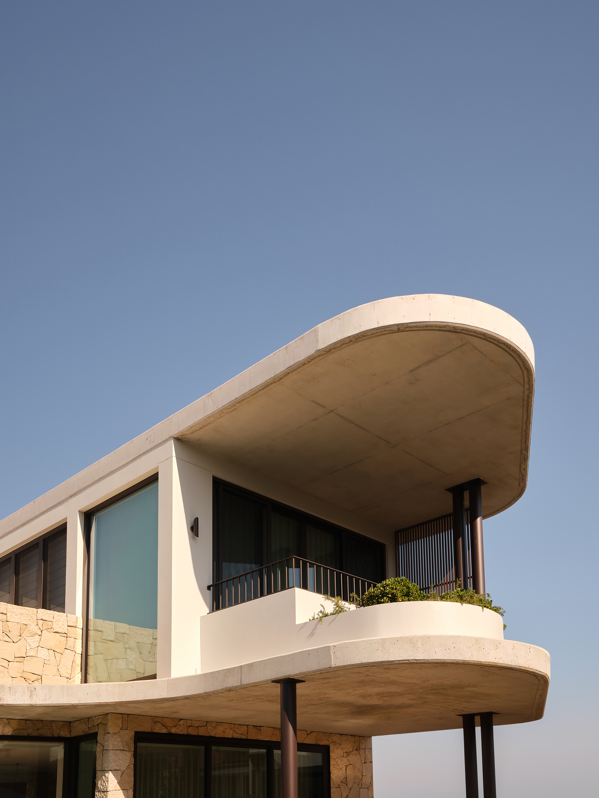 Cantilevered balcony with planted terrace railing and glazed openings below the curved concrete overhang at dusk