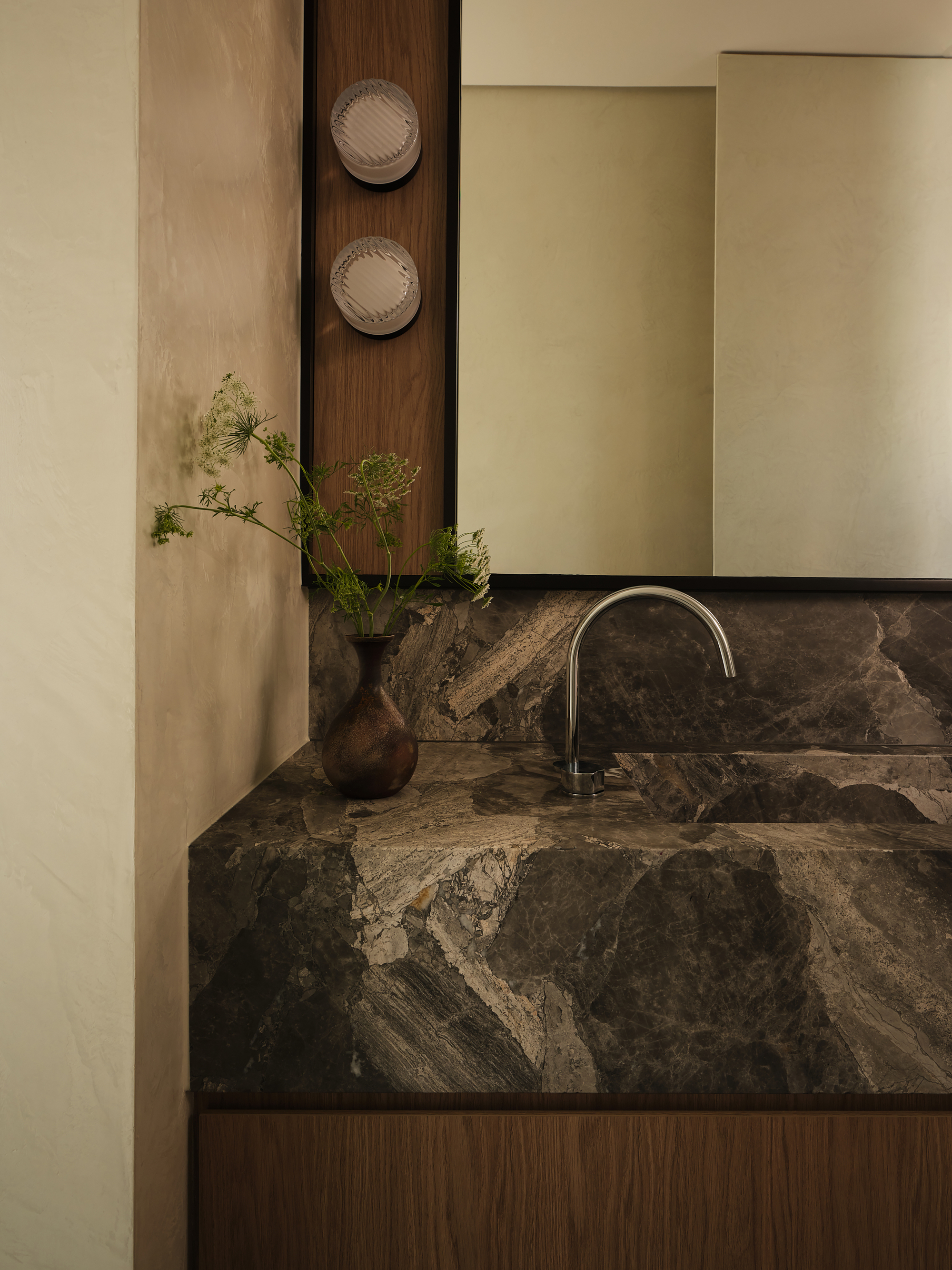 Bathroom vanity with dark veined stone countertop, integrated sink, and vase of green stems
