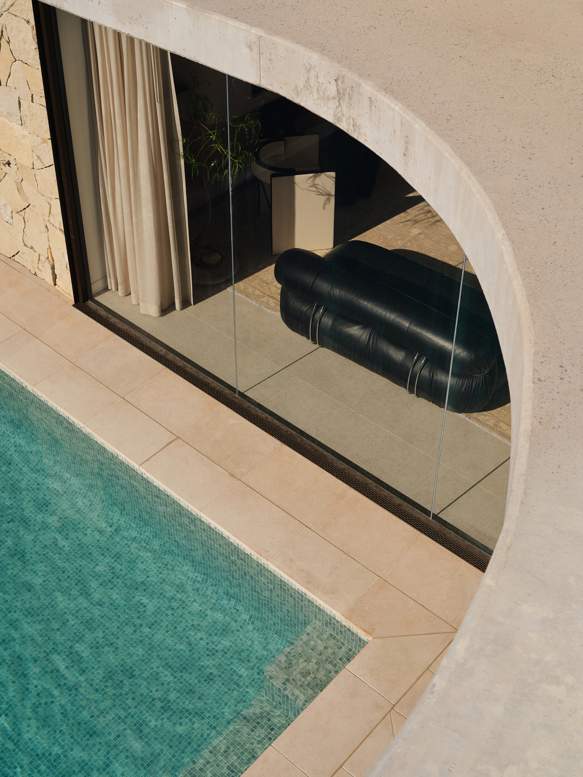 Curved pool edge with limestone coping and glass balustrade opening to interior living space