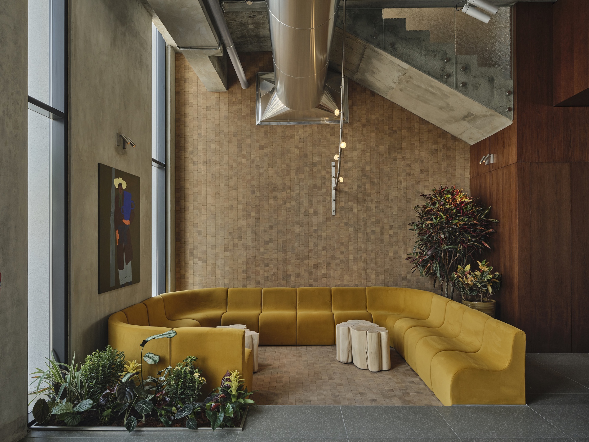 Double-height lobby with yellow sectional sofa beneath exposed concrete ceiling and ventilation ducts