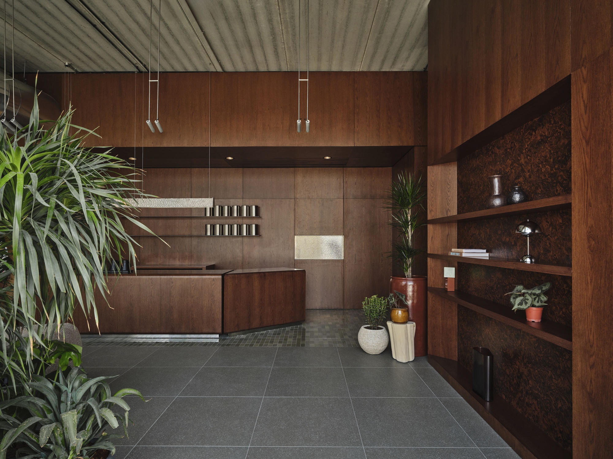 Reception desk with walnut cabinetry and cork-backed shelving adjacent to potted plants