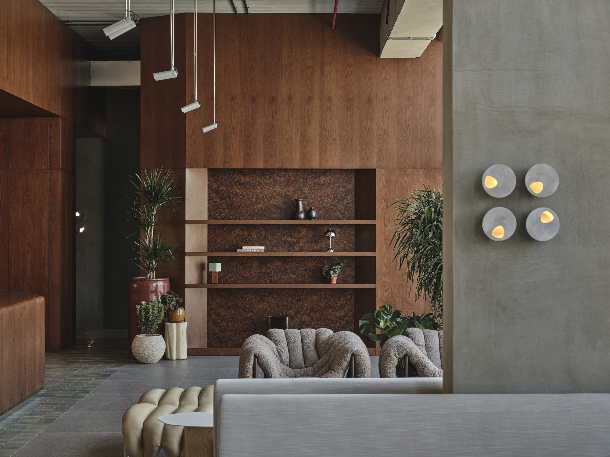Concrete wall with four circular sconces above seating area flanked by potted palms