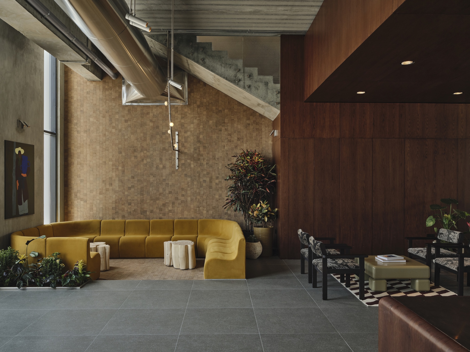 Double-height lobby with mosaic tile wall, exposed ductwork, and yellow curved sectional seating