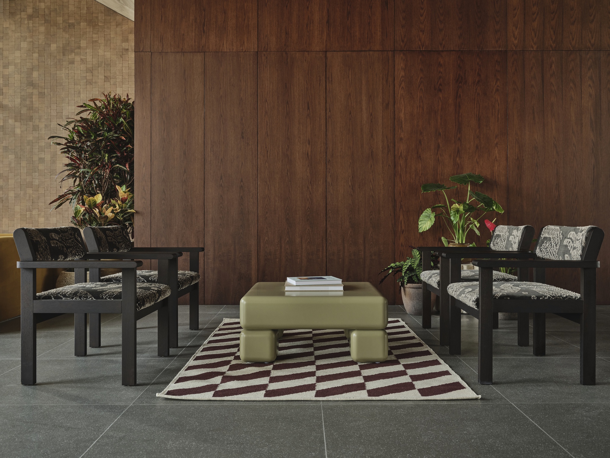 Seating arrangement with black timber chairs and pale ottoman on geometric rug against wood paneling