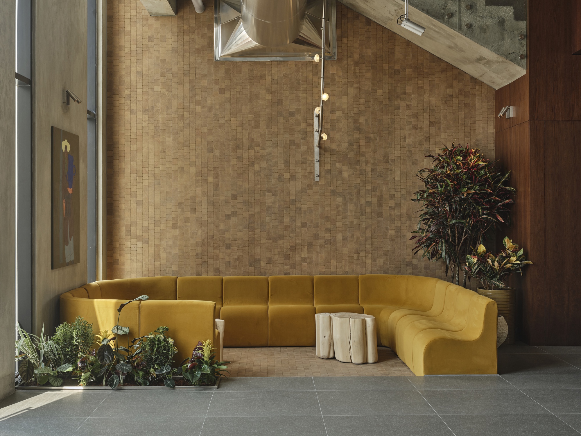 Corner view of the yellow sectional seating beneath suspended light fixture and exposed ceiling ducts