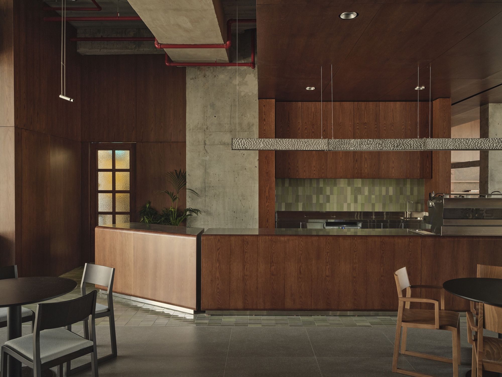 Kitchen counter with green mosaic backsplash, wooden cabinetry, and suspended woven light fixture overhead