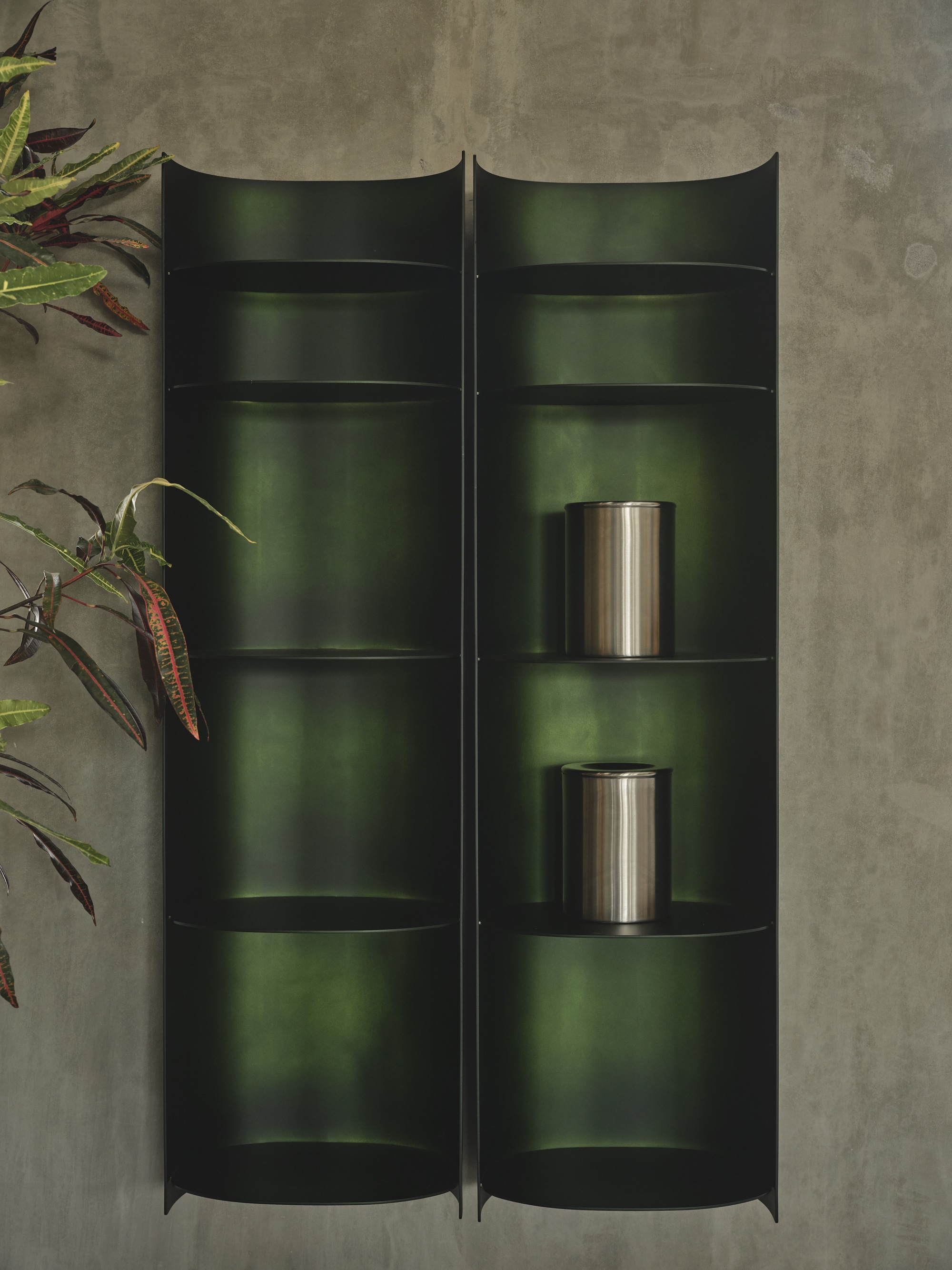 Top-down view of curved dark green metal shelving units with two stainless steel vessels and potted plants