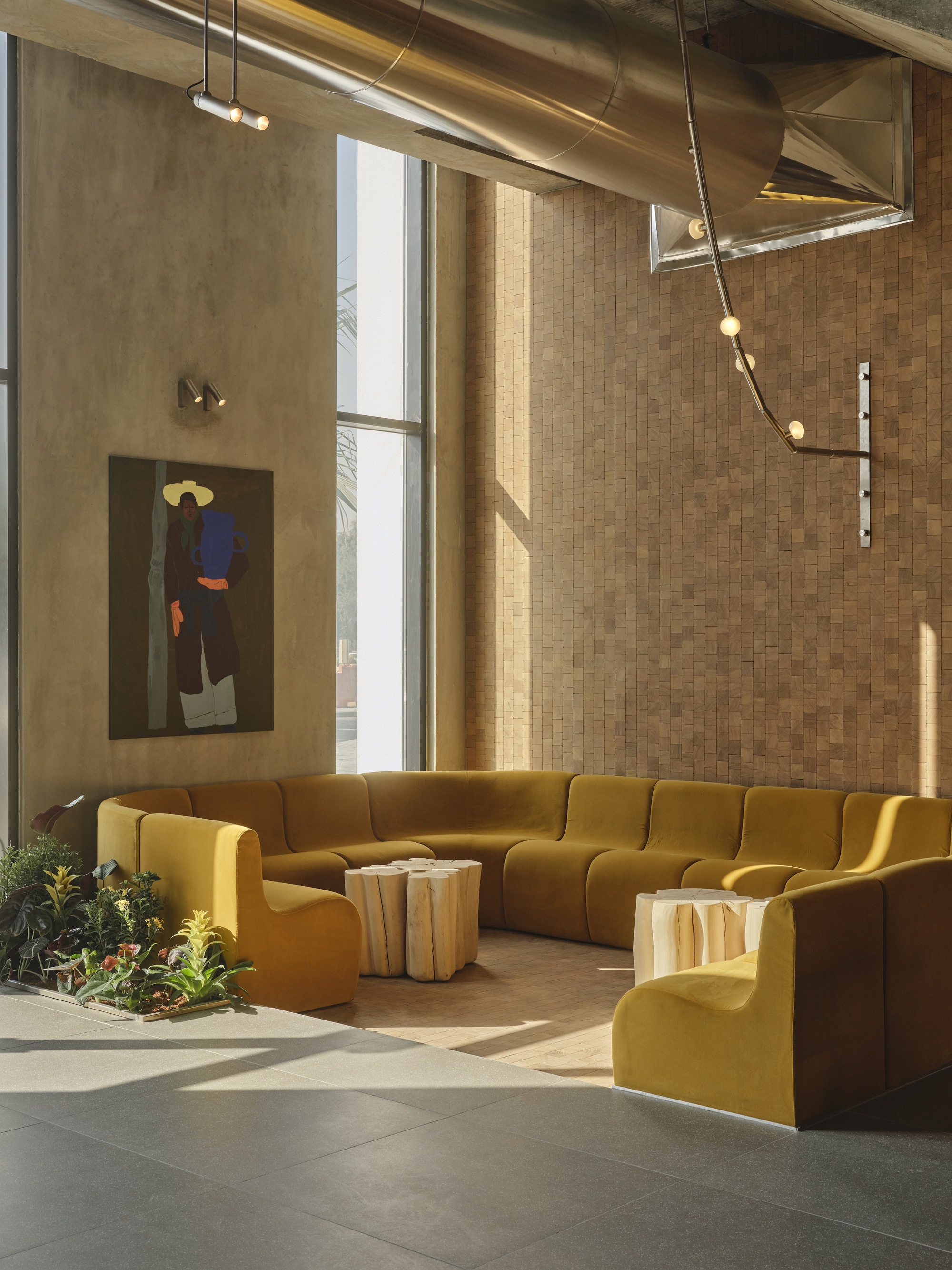 Double-height lounge with tall windows casting afternoon light across mustard upholstered seating and concrete floor