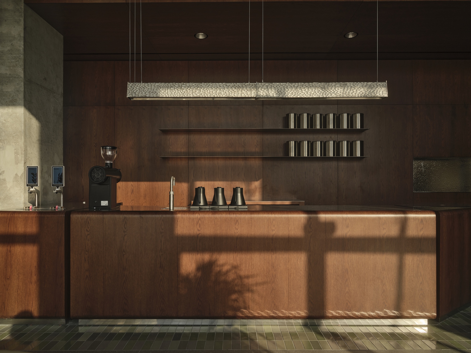 Wood-paneled counter with linear pendant light and open shelving in morning sunlight