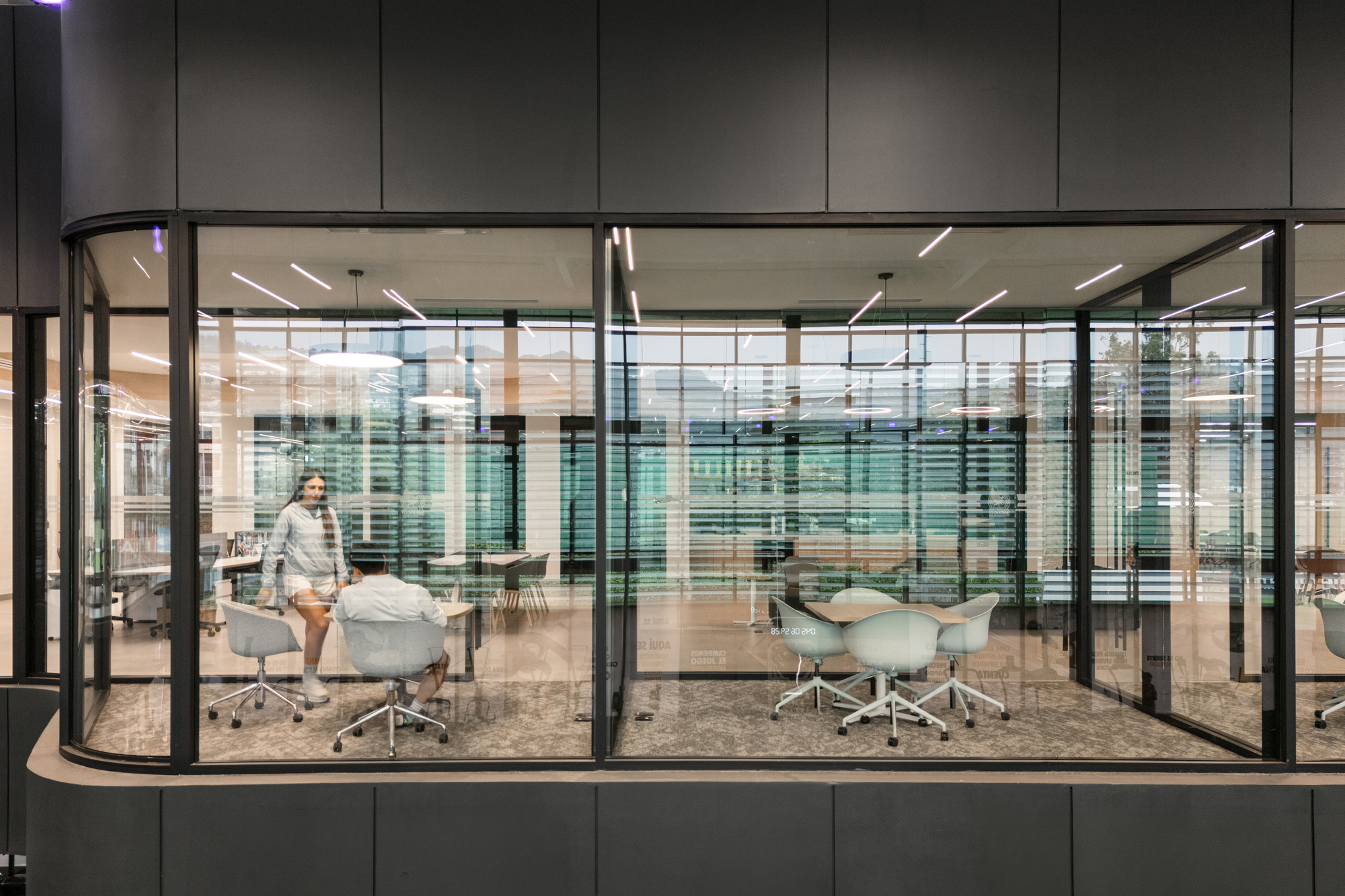 Curved glass-walled conference room with white task chairs and a figure moving past the glazed enclosure