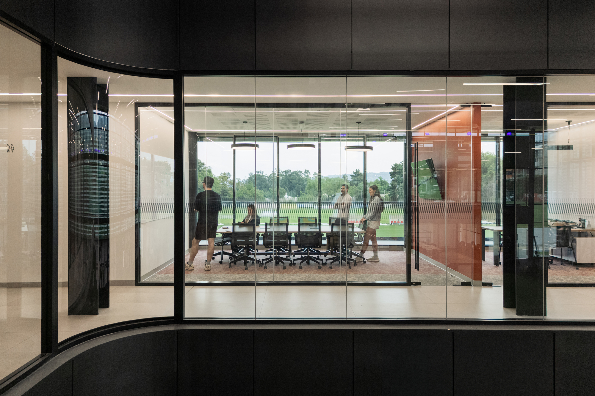 Glazed meeting room overlooking playing fields with pivoting copper door panel and figures inside