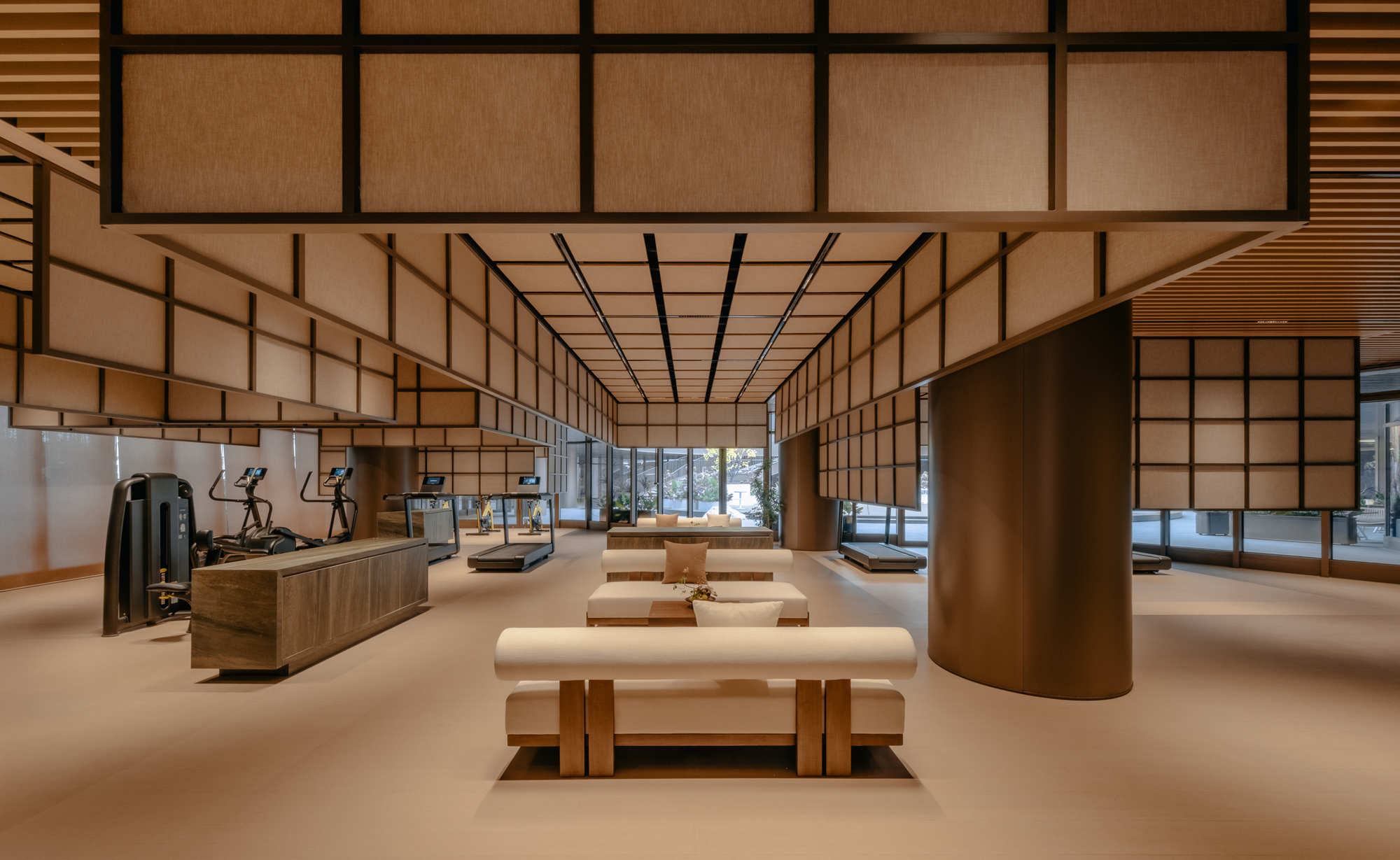 Fitness hall with translucent grid ceiling panels, timber benches, and bronze column wrapping