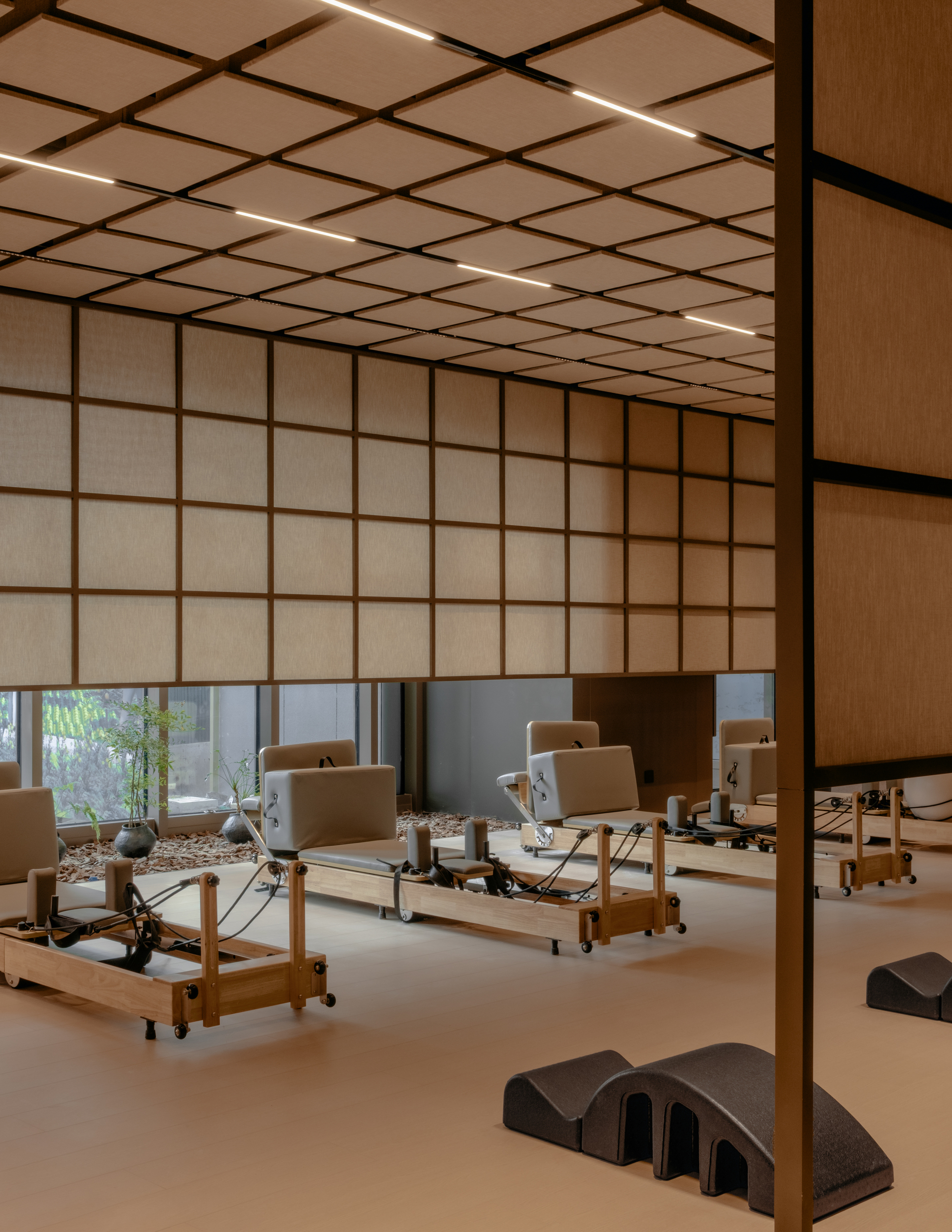 Interior studio with translucent grid screens, wood slat ceiling panels, and Pilates reformer equipment on pale flooring
