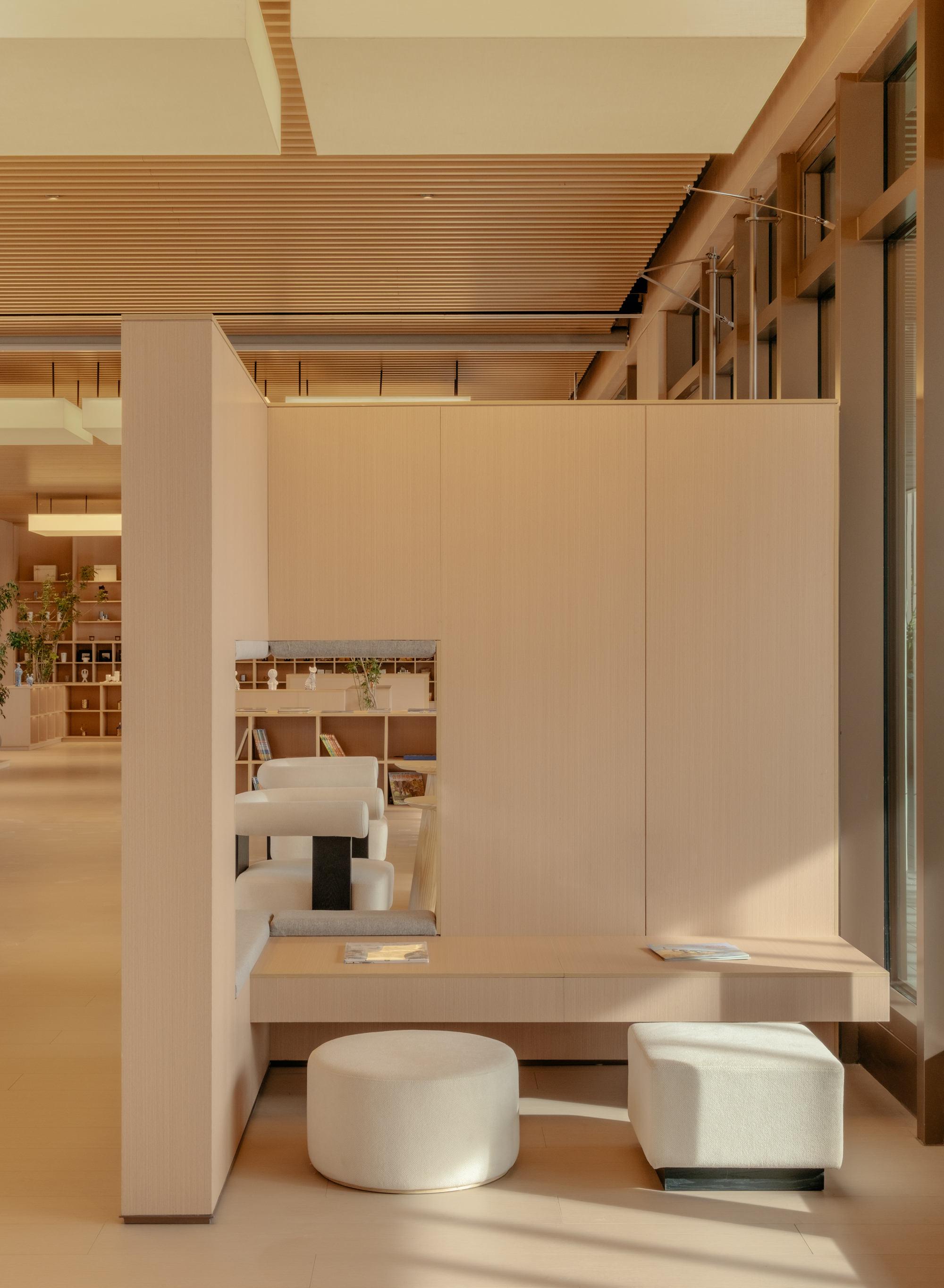 Reading nook with pale timber desk, round upholstered stools, and architectural model on display
