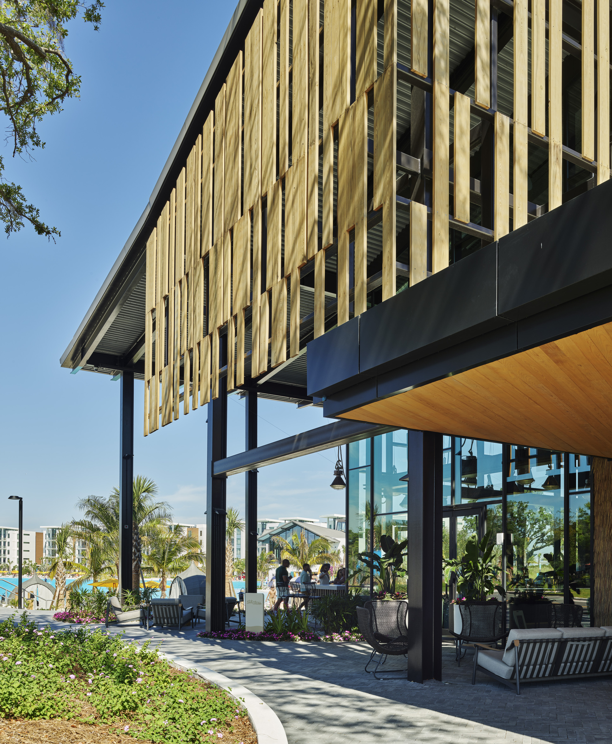 Covered terrace with steel columns and timber soffit beneath a cantilevered upper level clad in vertical slats
