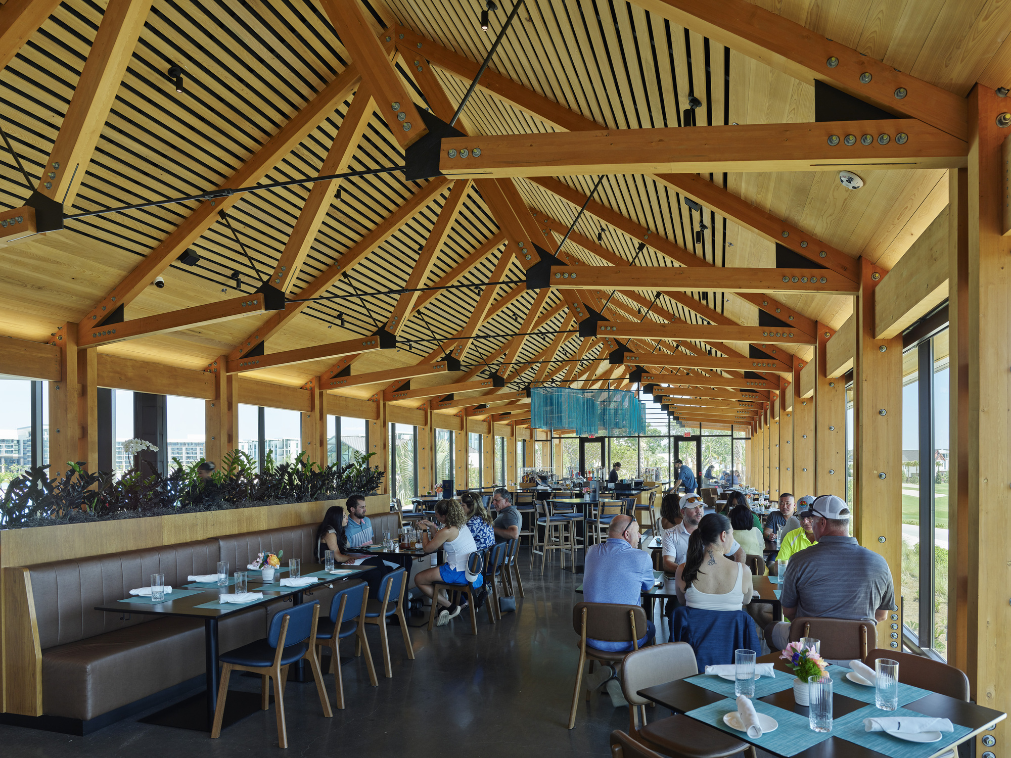 Dining hall with exposed timber trusses and slatted ceiling panels over tables filled with seated guests