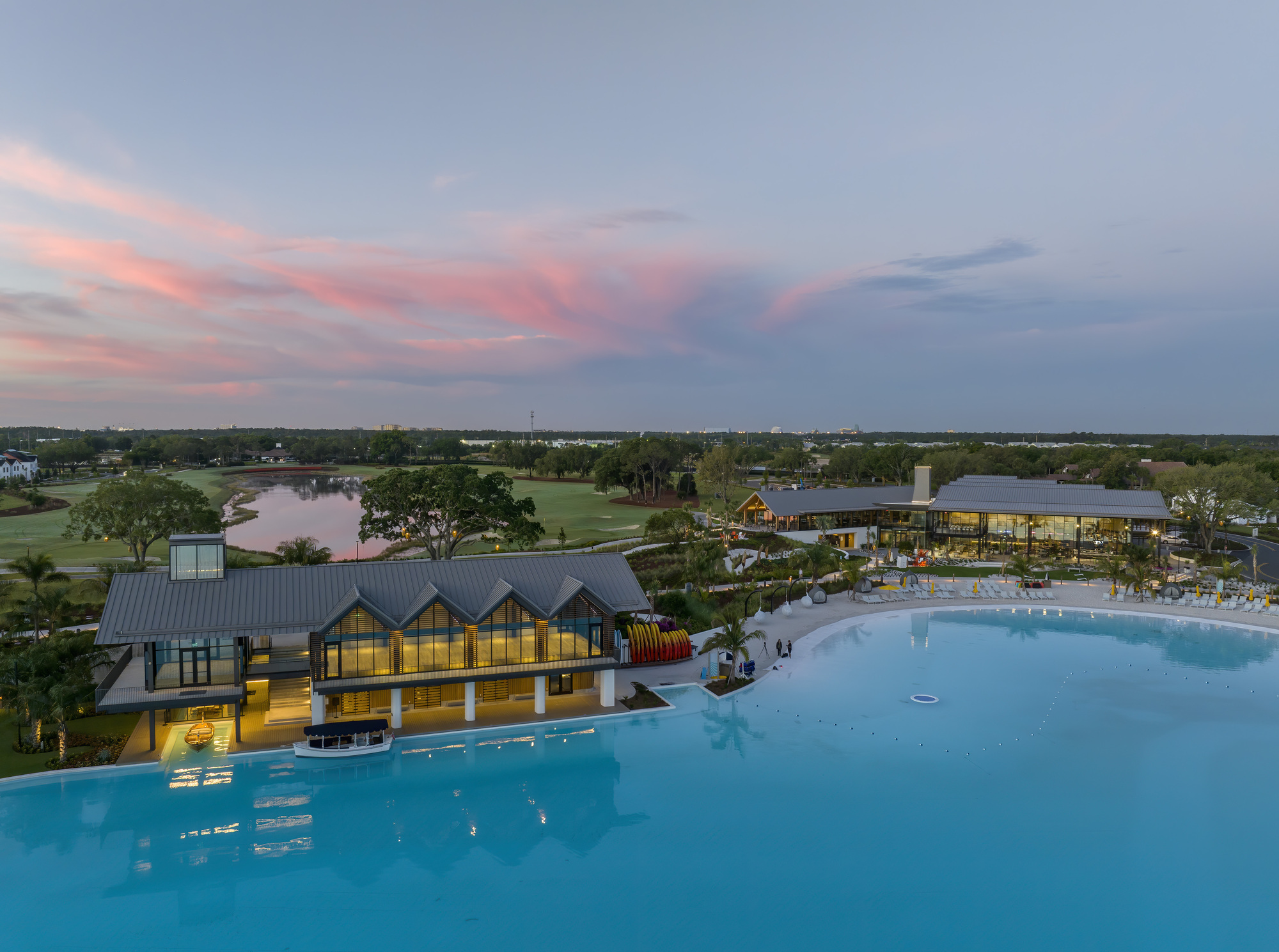Aerial view of poolside pavilion with gabled roofs and lakeside golf course at dusk