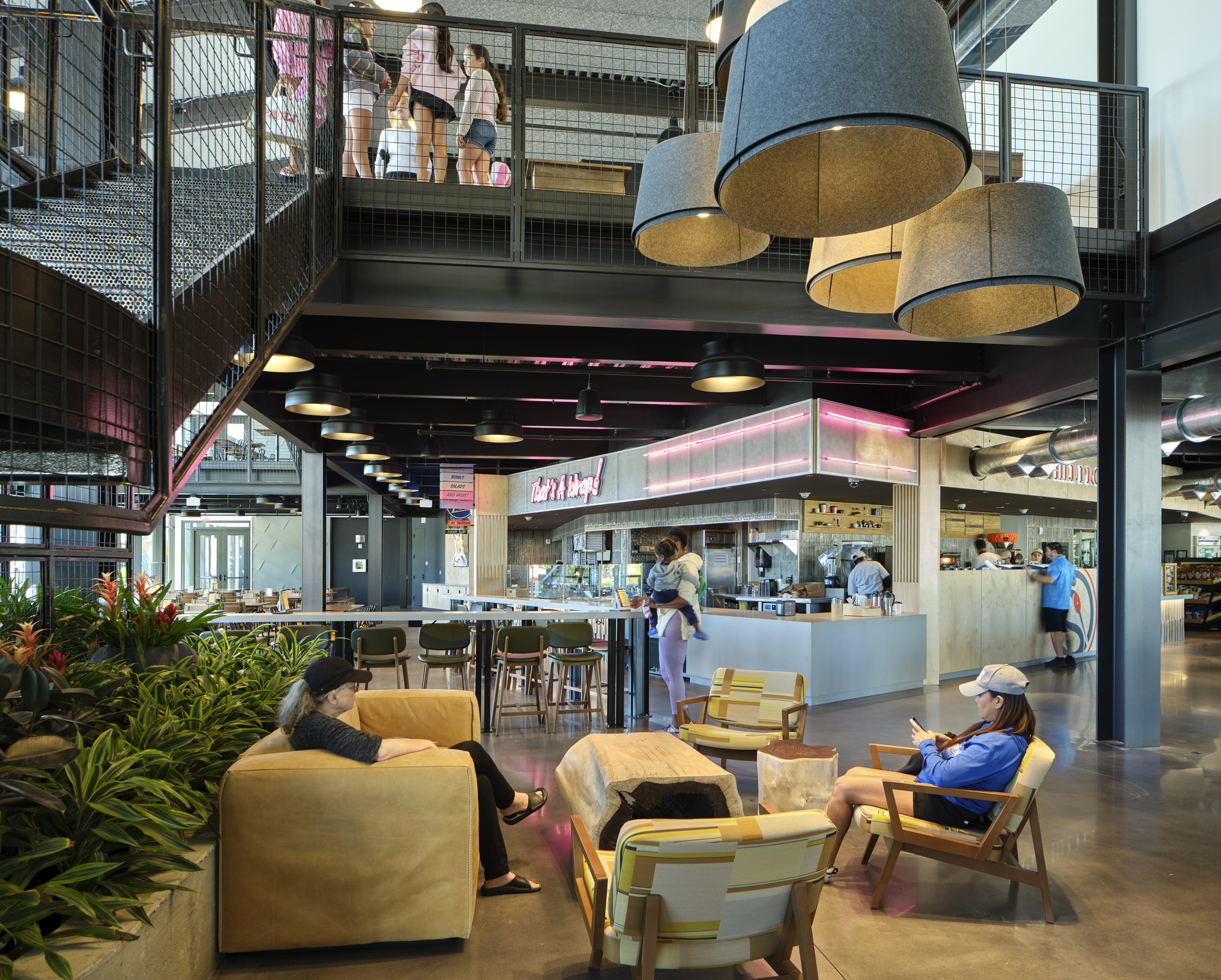 Double-height interior with mezzanine, wire mesh railings, pendant lighting and seating area below upper walkway
