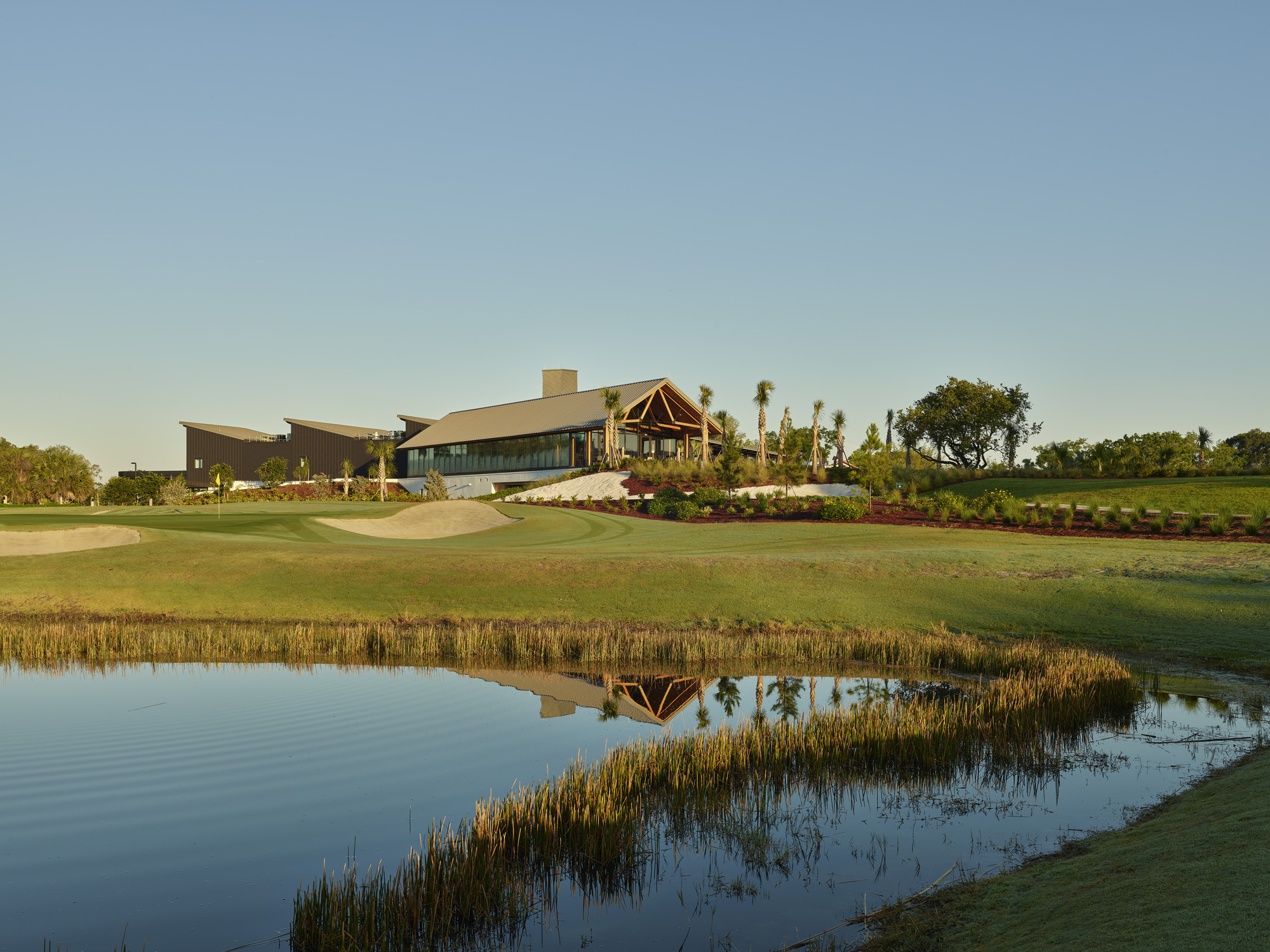 Clubhouse complex viewed across golf course water hazard with reedy shoreline in late afternoon light