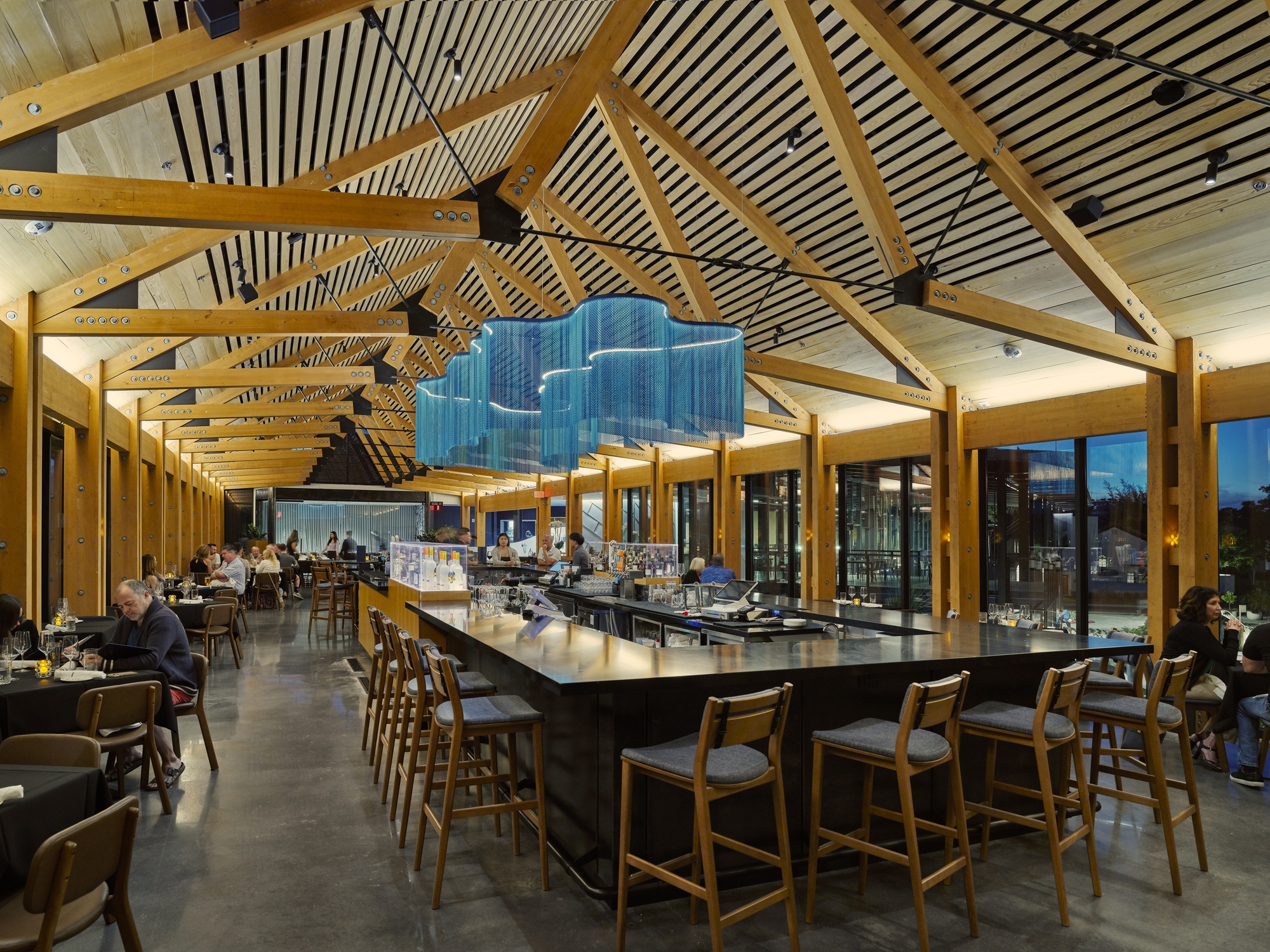 Interior dining space with exposed timber trusses and striped ceiling panels above a central bar counter