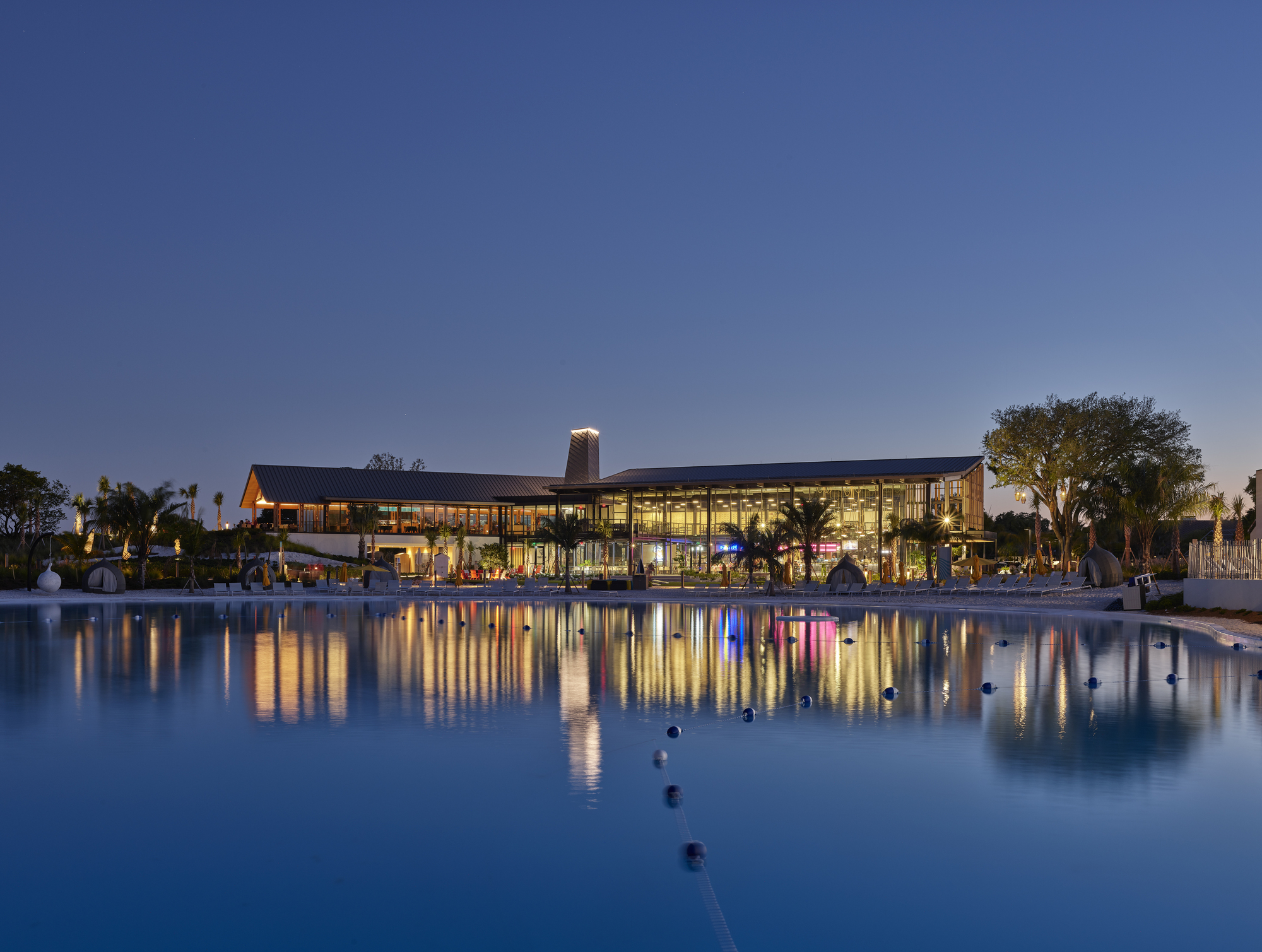 Glazed pavilion reflected in a pool at blue hour with fountain jets and palm trees