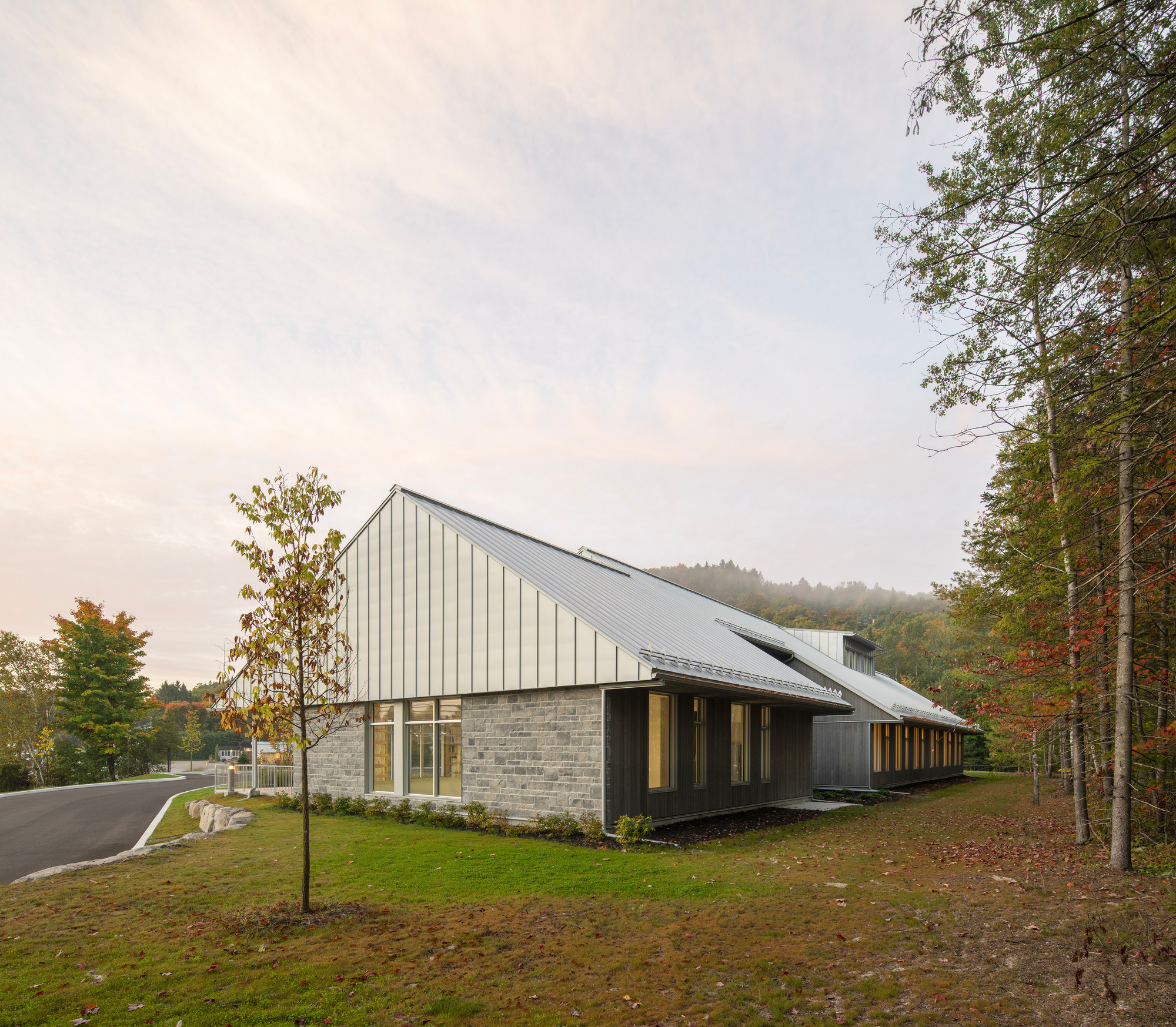 Stone base and standing-seam metal roof seen from a grassy clearing edged by autumn trees