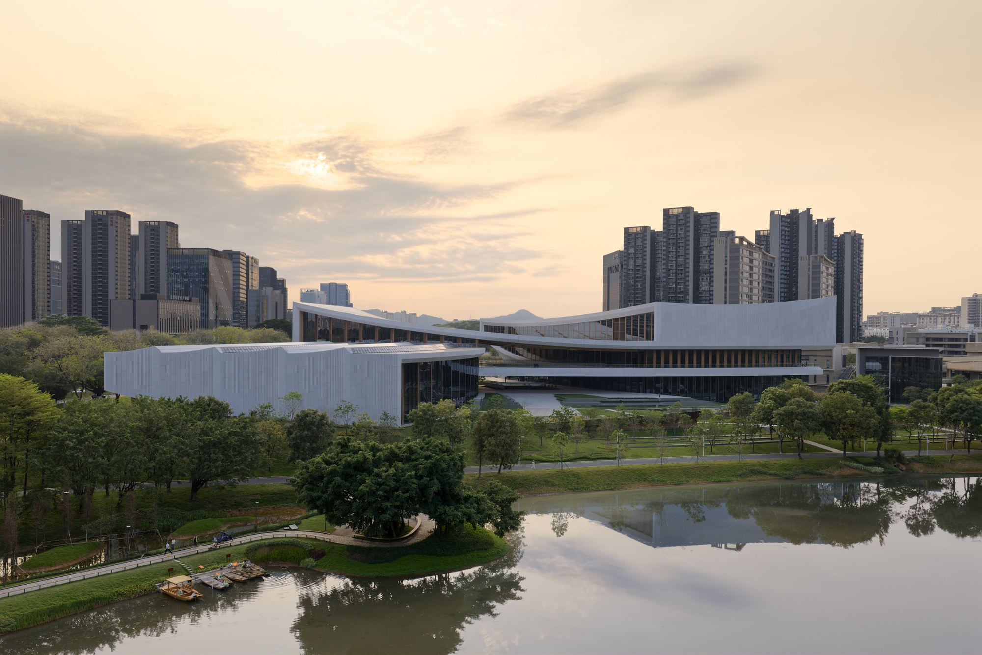 Aerial view of the white cultural center with layered rooflines beside a reflecting pond at dusk
