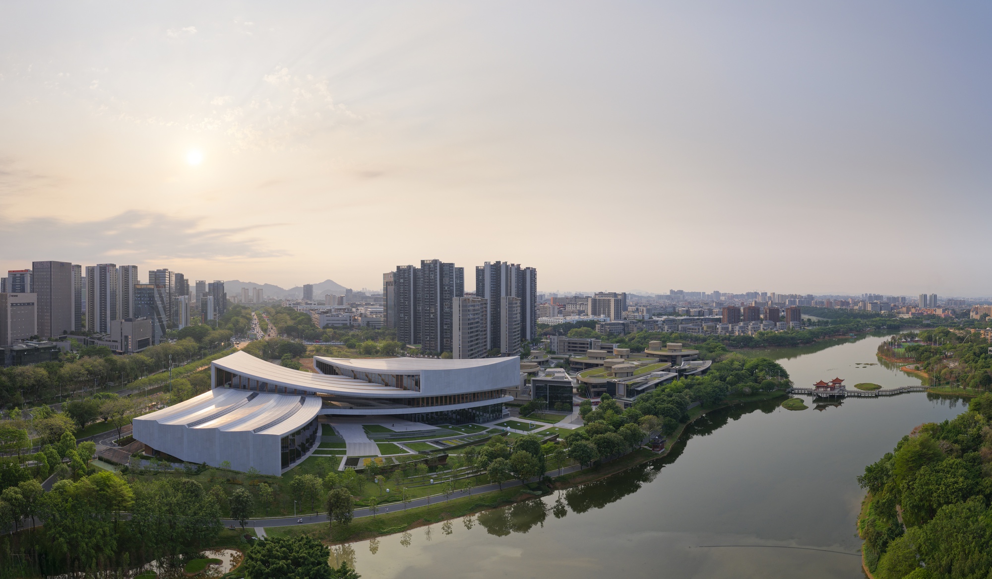 Wide view showing the curved volumes and horizontal louvers of the riverside complex at sunset