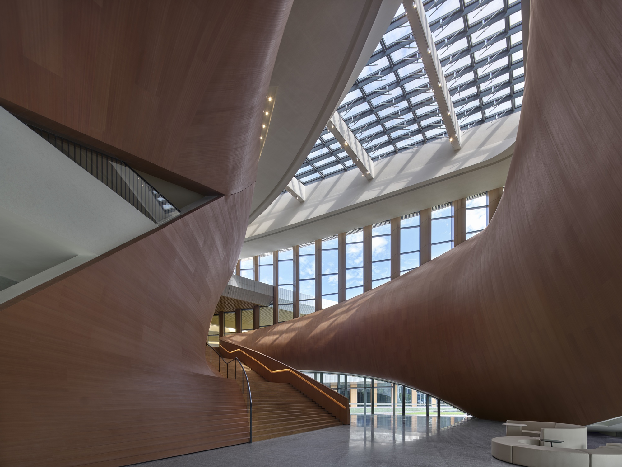Interior atrium with timber-clad staircase rising beneath a geometric skylight with angular glazed openings