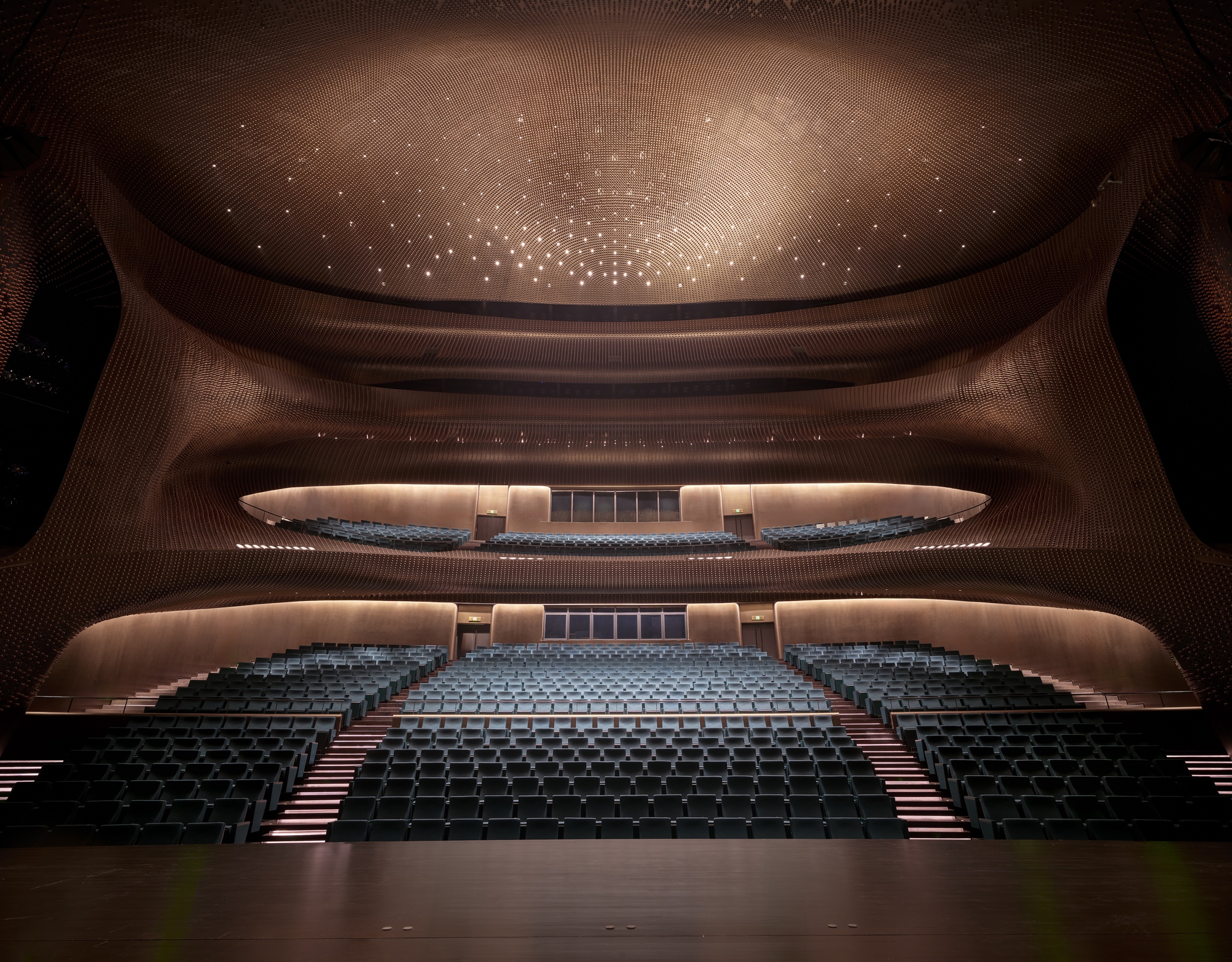 Theater auditorium with tiered seating facing curved balconies and starlit perforated dome ceiling