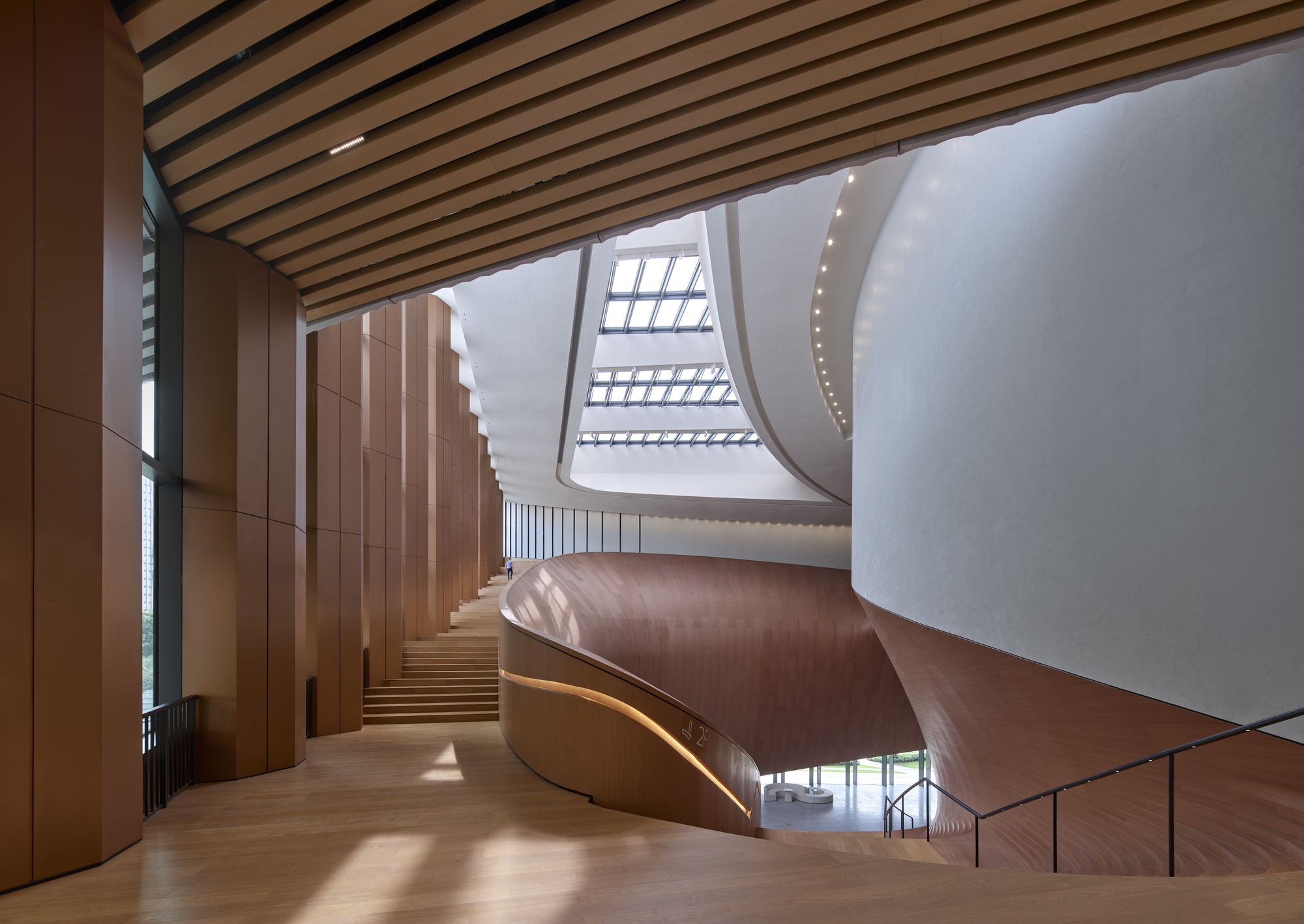 Interior view of the helical timber-clad staircase rising beneath a skylit atrium with timber batten ceiling