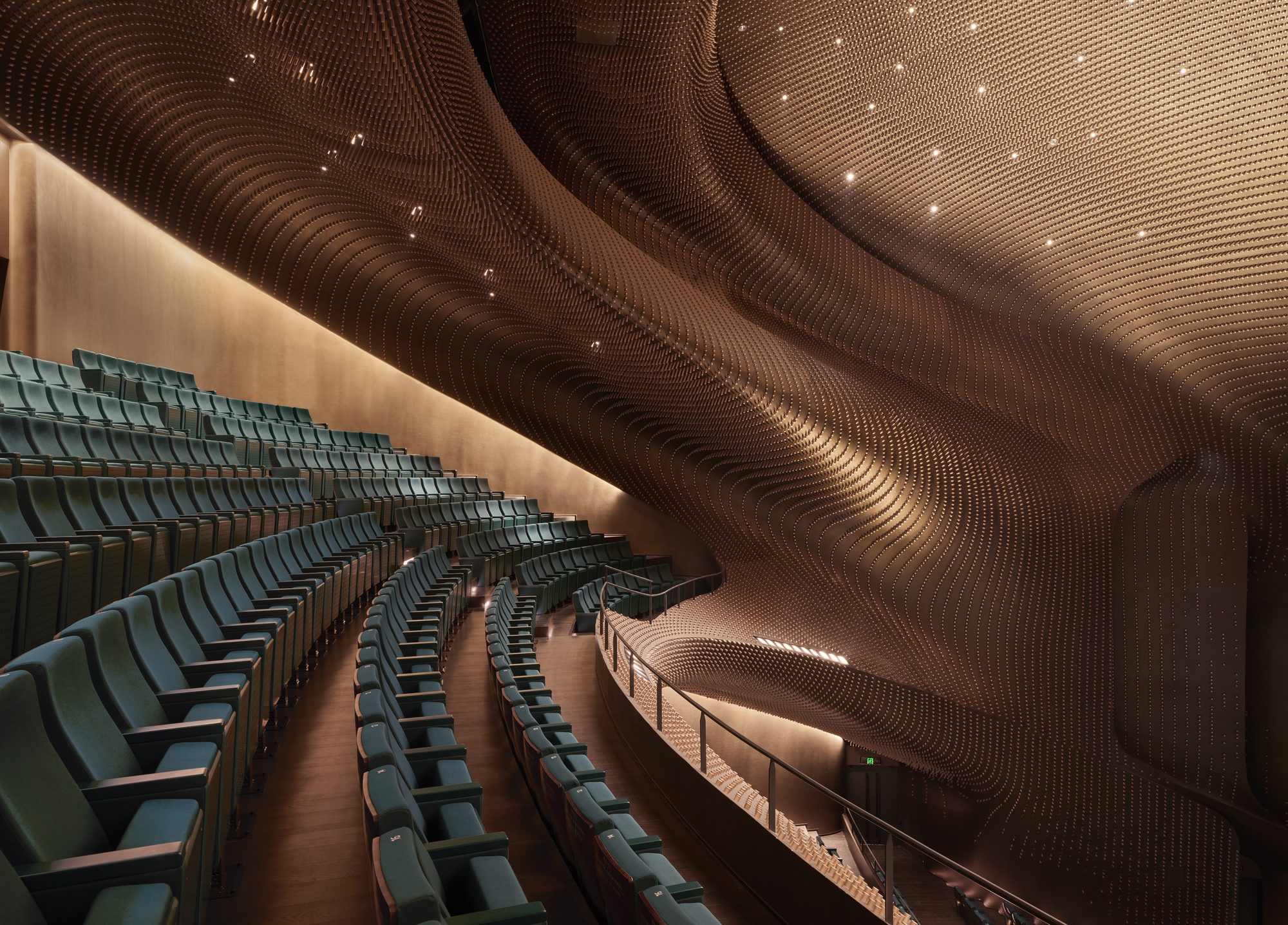 Raked seating and balcony beneath a flowing timber ceiling with integrated recessed spotlights