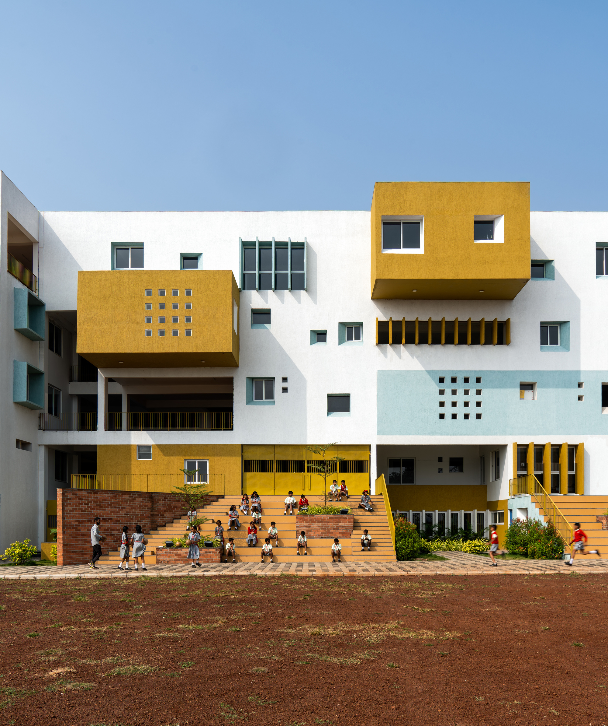 Facade overlooking the steps and courtyard filled with children in uniform gathering outside