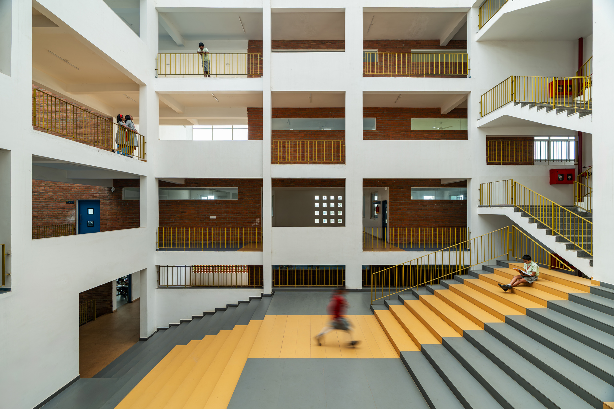 Interior atrium with stacked openings, yellow and gray tiered steps and a child in motion
