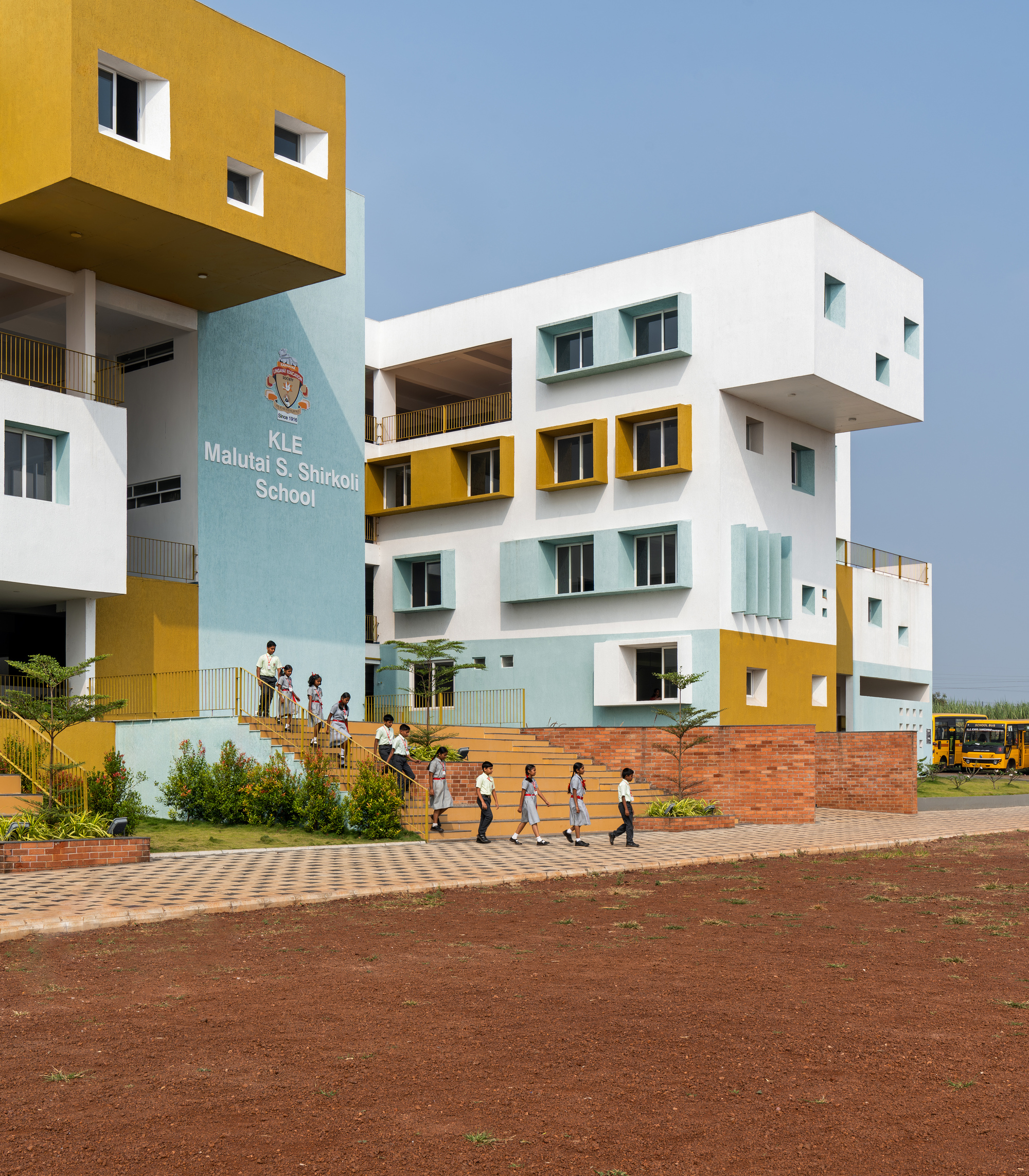 Street view of the stacked white and yellow volumes with students walking on the brick-paved courtyard