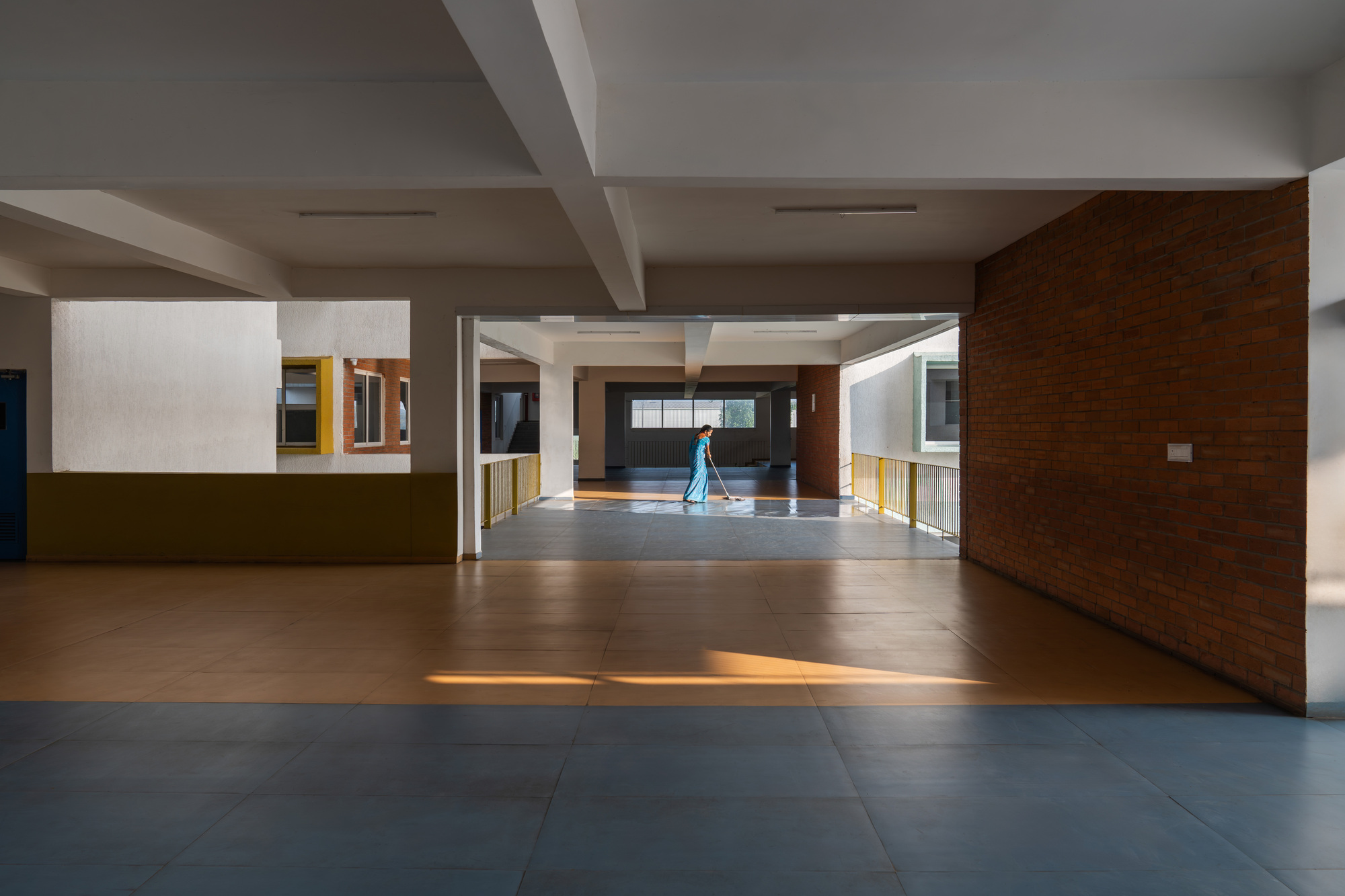 Interior hallway with grey floor tiles and exposed brick wall as a figure walks through connecting spaces