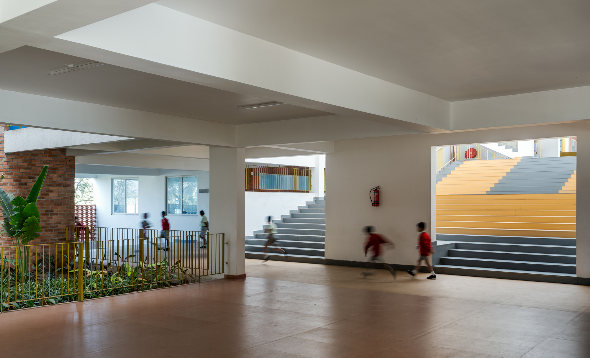 Circulation space with planted beds behind yellow railings as students move past a wide staircase